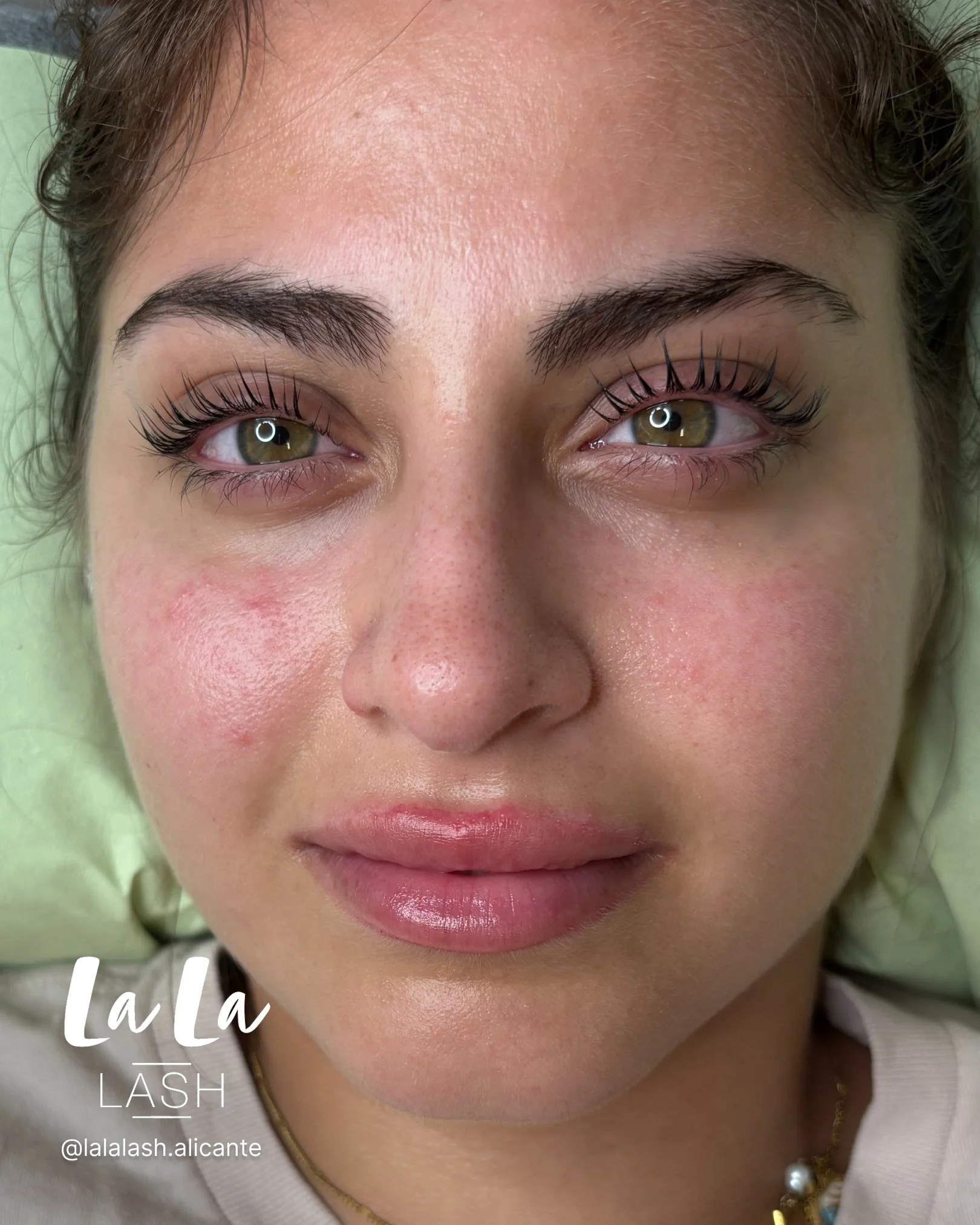 Primer plano de rostro de mujer con pestañas postizas y cejas arregladas. Fundo color verde suave.