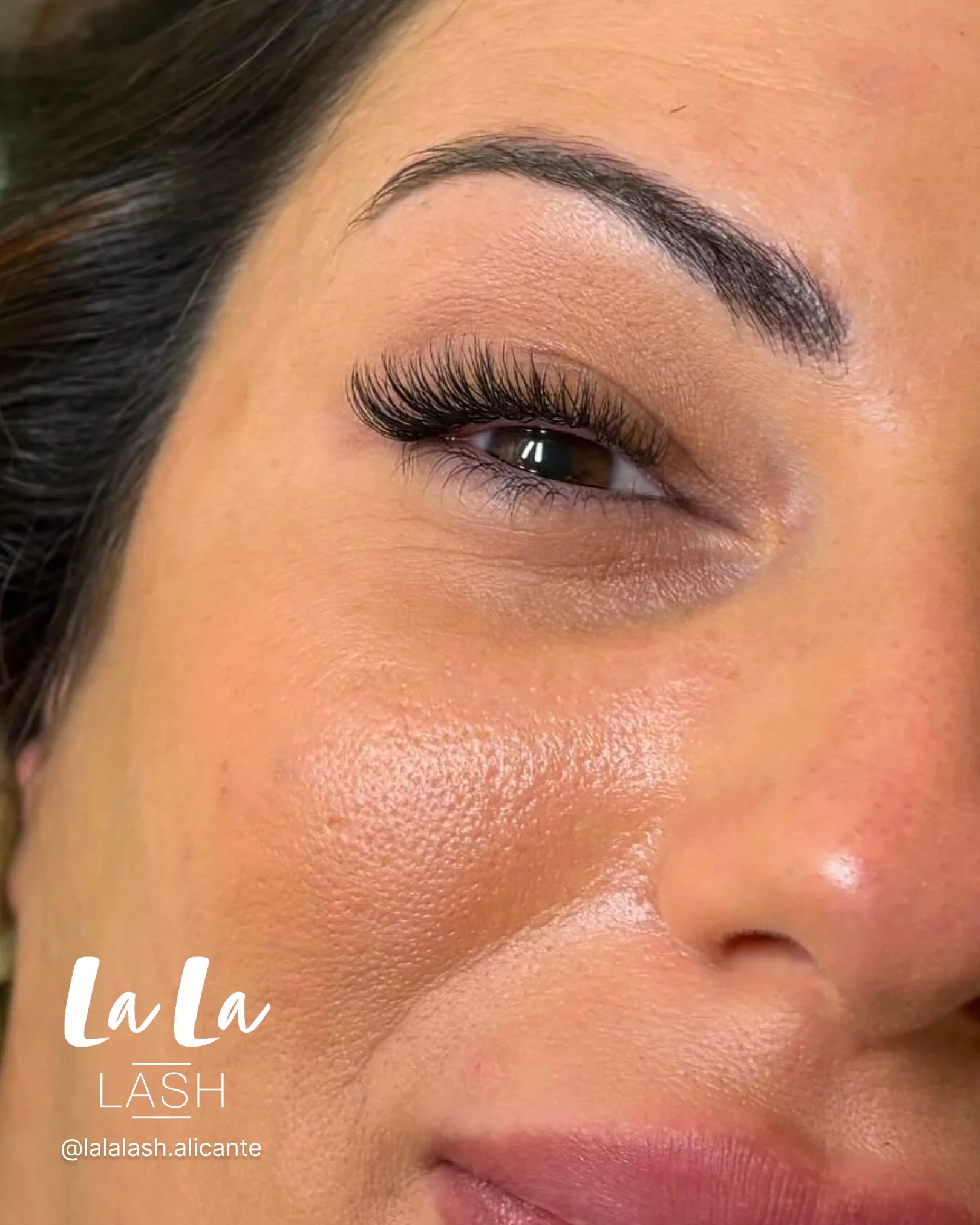 Cerca de un ojo con pestañas postizas, ceja perfectamente delineada y piel bien cuidada, con maquillaje natural y iluminación suave.