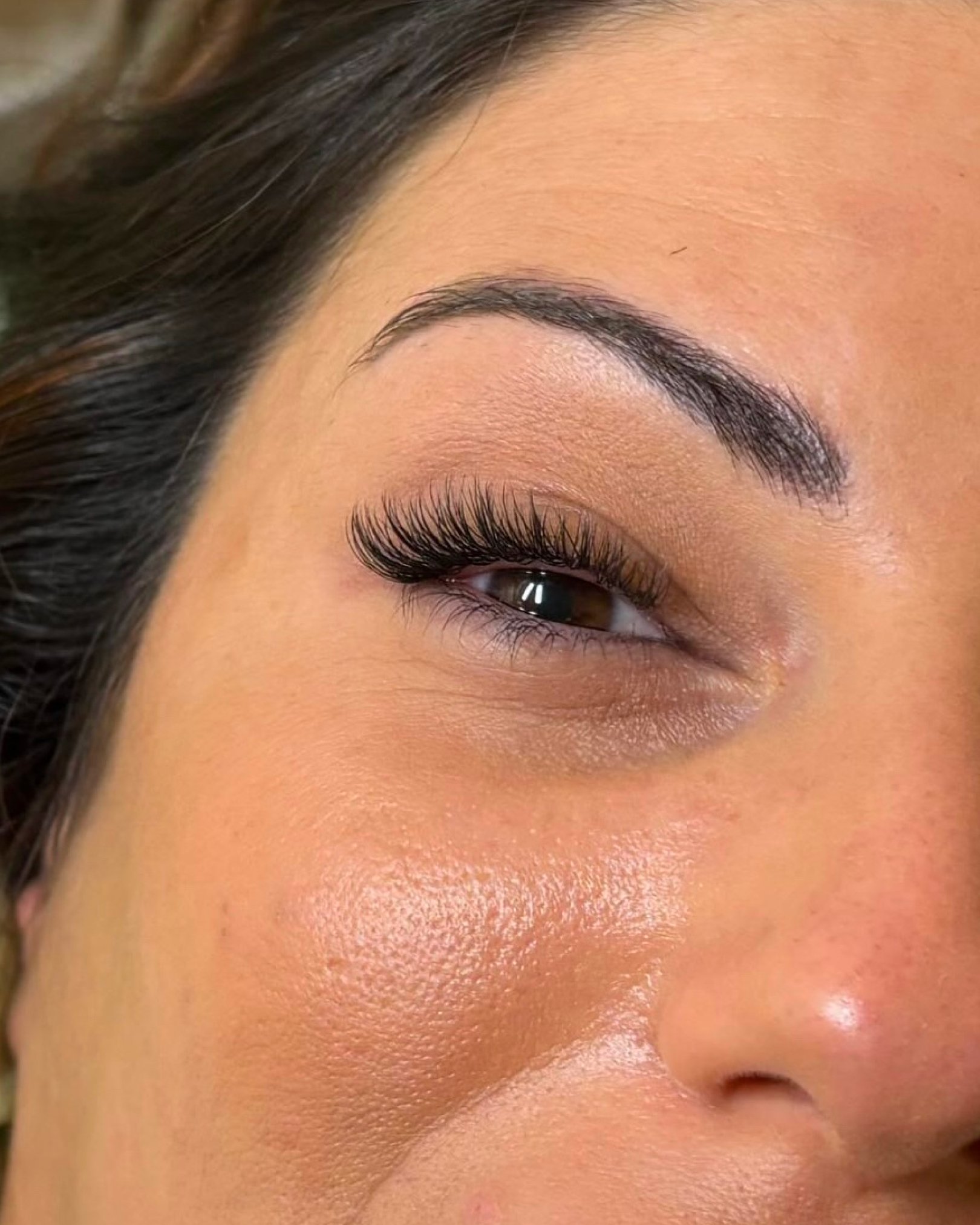 Cerca de la frente, un ojo cerrado con pestañas largas y ceja bien definida, piel suave y bronceada.