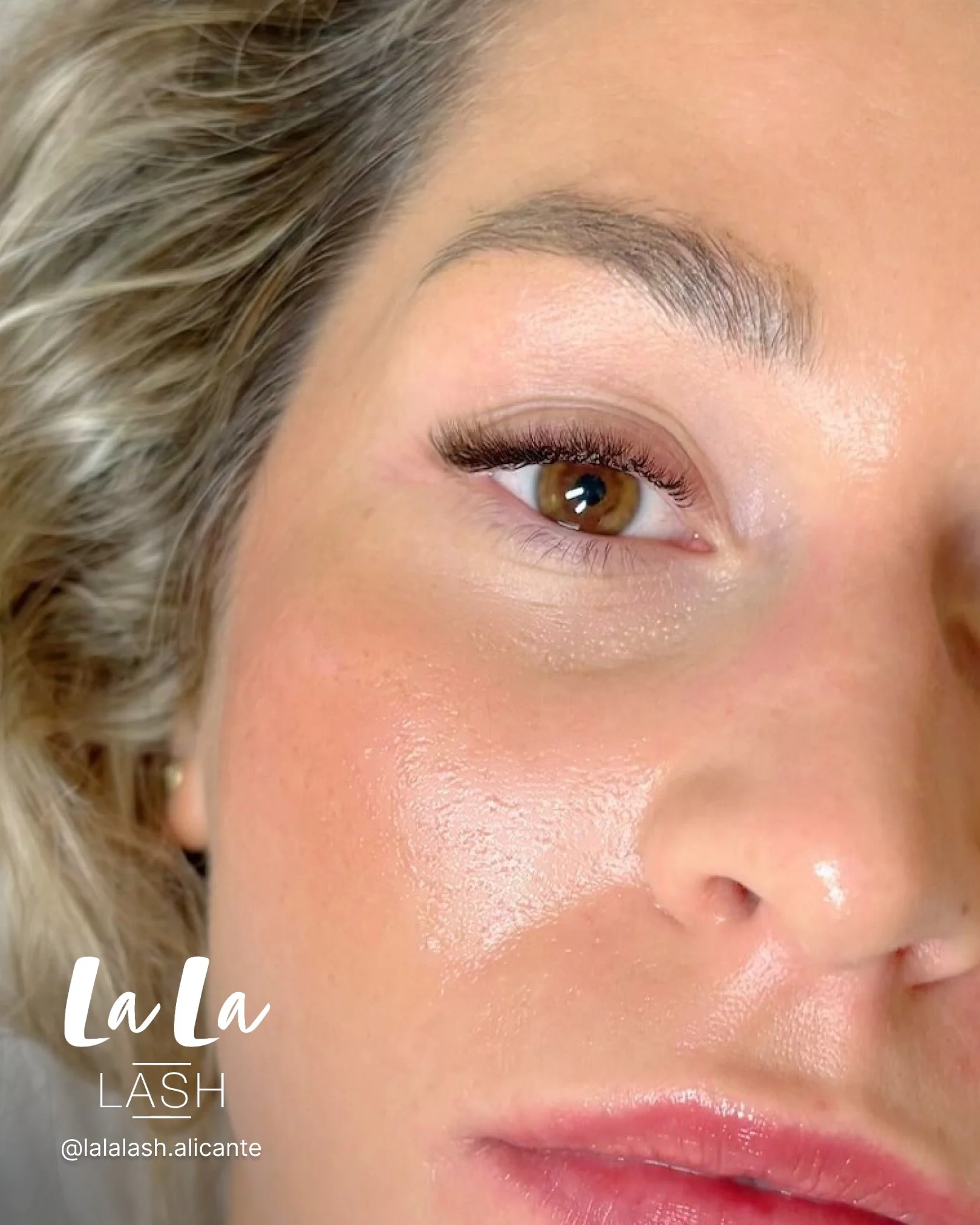 Primer plano de un ojo de mujer con maquillaje en las pestañas y ceja claramente definida, cabello rubio ondulado, piel brillante y labios rosados. Texto en la imagen que dice 'La La' y 'Lash'.