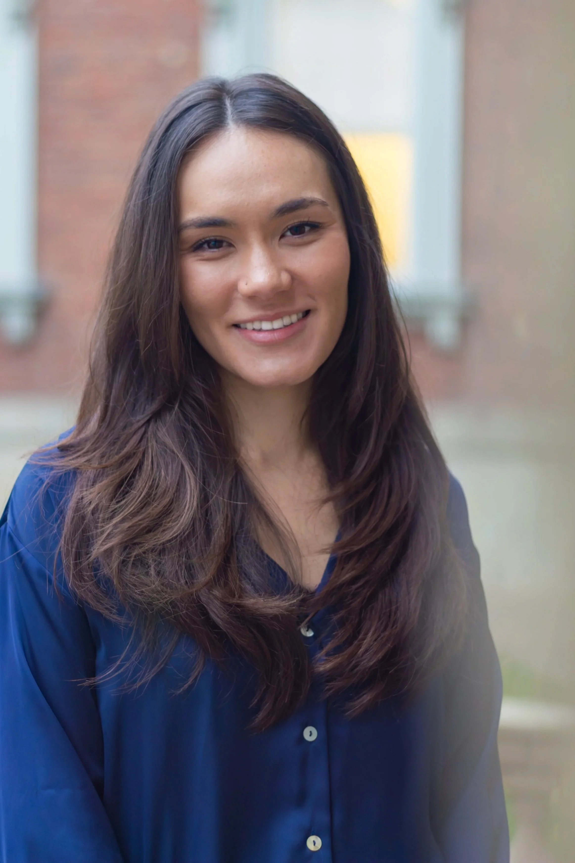 A young woman with long dark hair smiling outdoors, wearing a navy blue shirt.