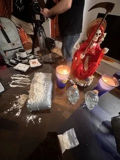 Table with a red Santa Claus decoration, candles, powdered substances, and various objects.