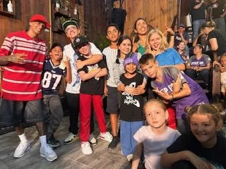 Group of children and teenagers posing indoors, some making peace signs and smiling.