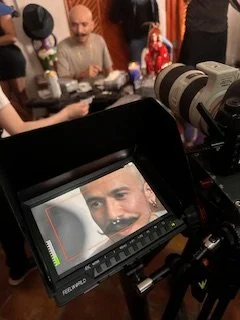 Close-up of a professional camera's viewfinder showing a person smiling and looking directly at the camera in a behind-the-scenes setting.