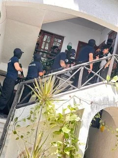 Eight police officers walking along a balcony outside a building, with bookshelves visible inside.