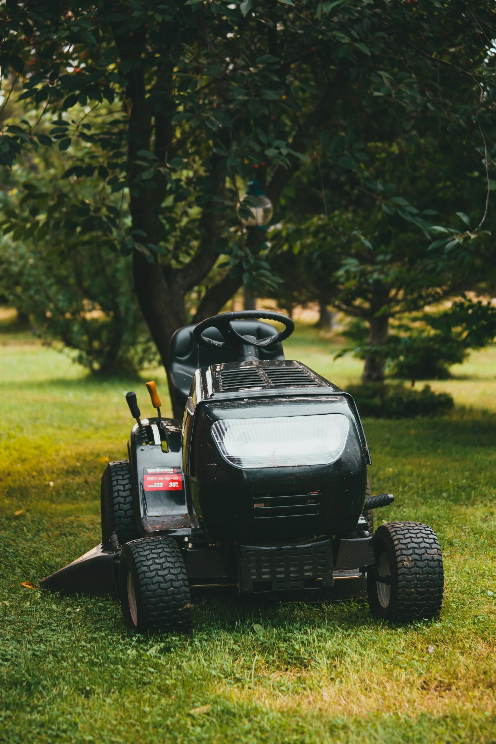Black riding lawn mower on grass with trees in the background.