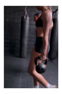A woman in workout clothes holding  kettlebells doing a farmers carry for HYROX Salt Lake City.