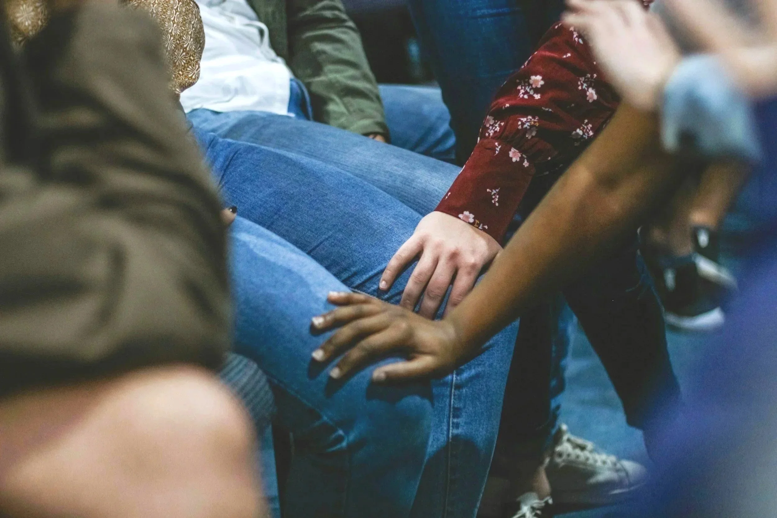 People sitting closely together, with one person's hand resting on another person's knee, in a group setting.