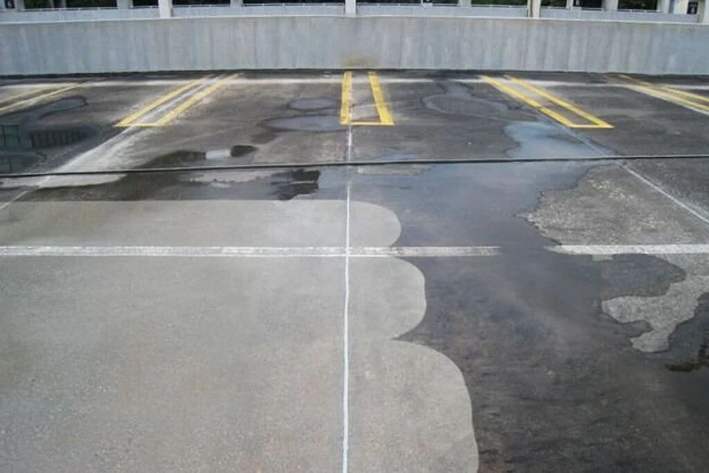 Newly painted parking space lines in a parking lot, with some areas of the pavement covered in old paint and patches.