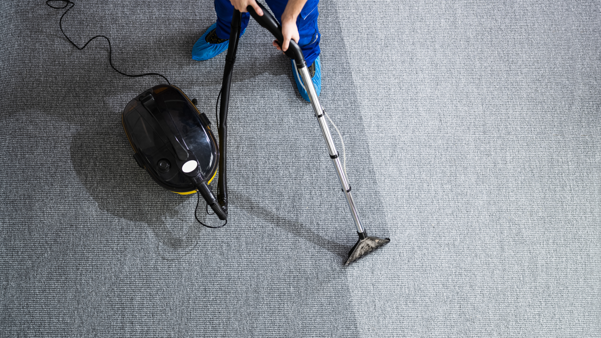 A person using a yellow and black carpet cleaner on a grey carpet floor.