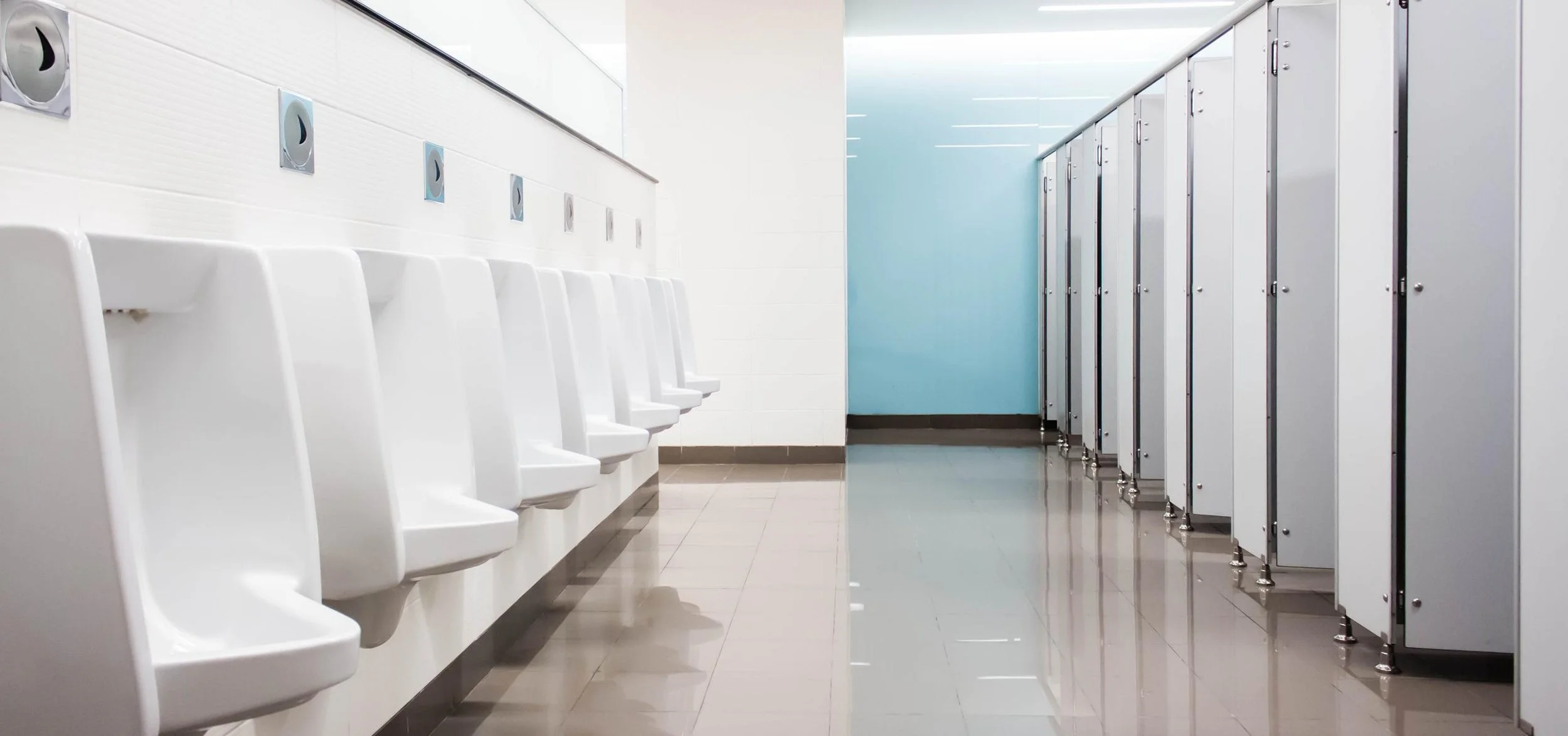 Public restroom with white urinals on the left wall and blue stall doors on the right side.
