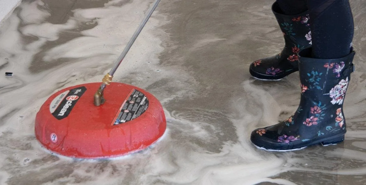 Person wearing black rain boots with floral pattern standing in shallow water near a red wet/dry vacuum cleaner.