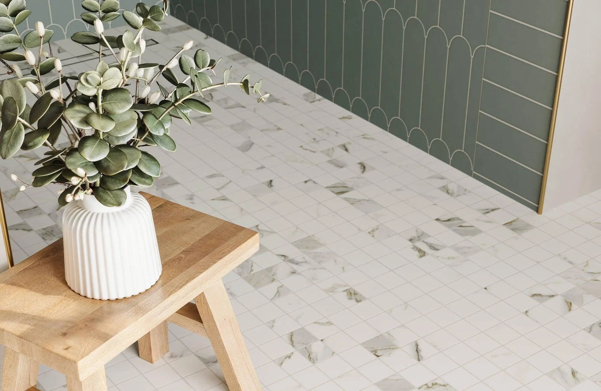 A white ribbed ceramic vase with greenery on a wooden table, with a tiled floor and geometric patterned wall in the background.