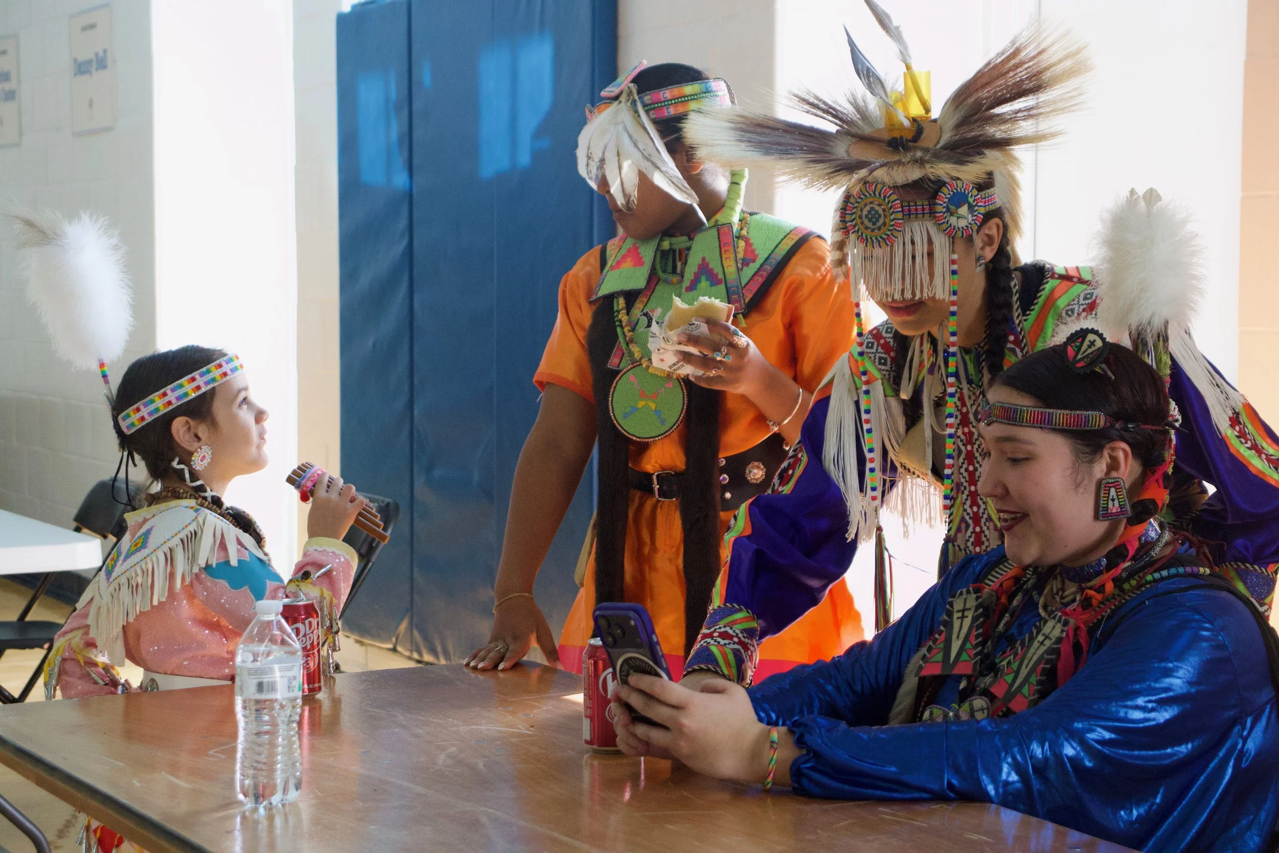 Amonitey and her cousin, Cristian, look through photos and videos of their dancing to the side of the dance floor as two other children share snacks in the background at the Carolina Indian Circle Pow Wow at the University of North Carolina at Chapel