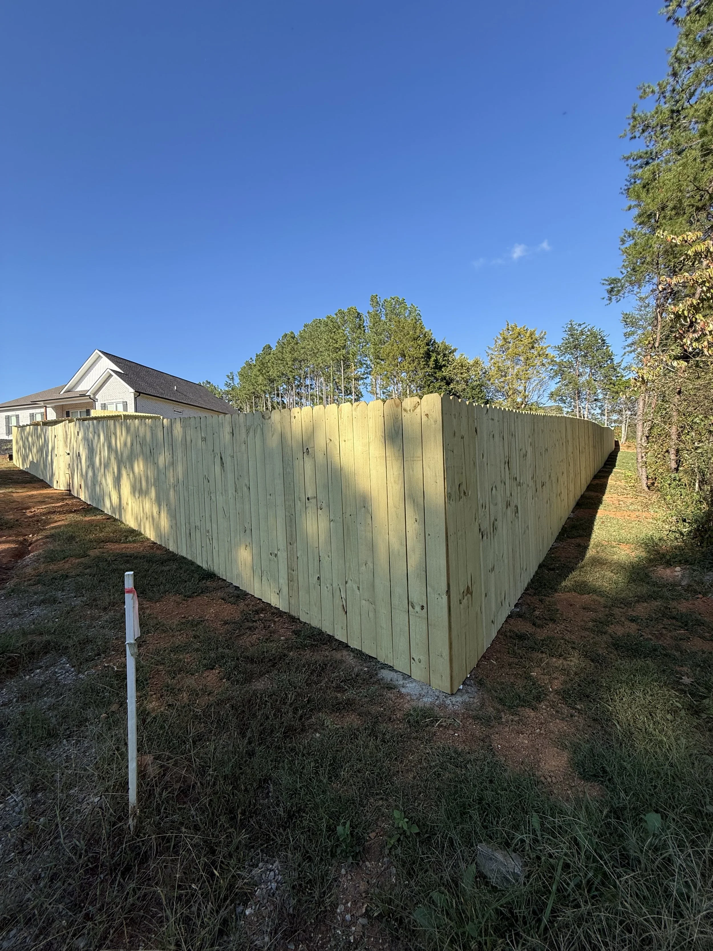 A wooden privacy fence installed along a corner of a residential yard with a house in the background and a clear blue sky.