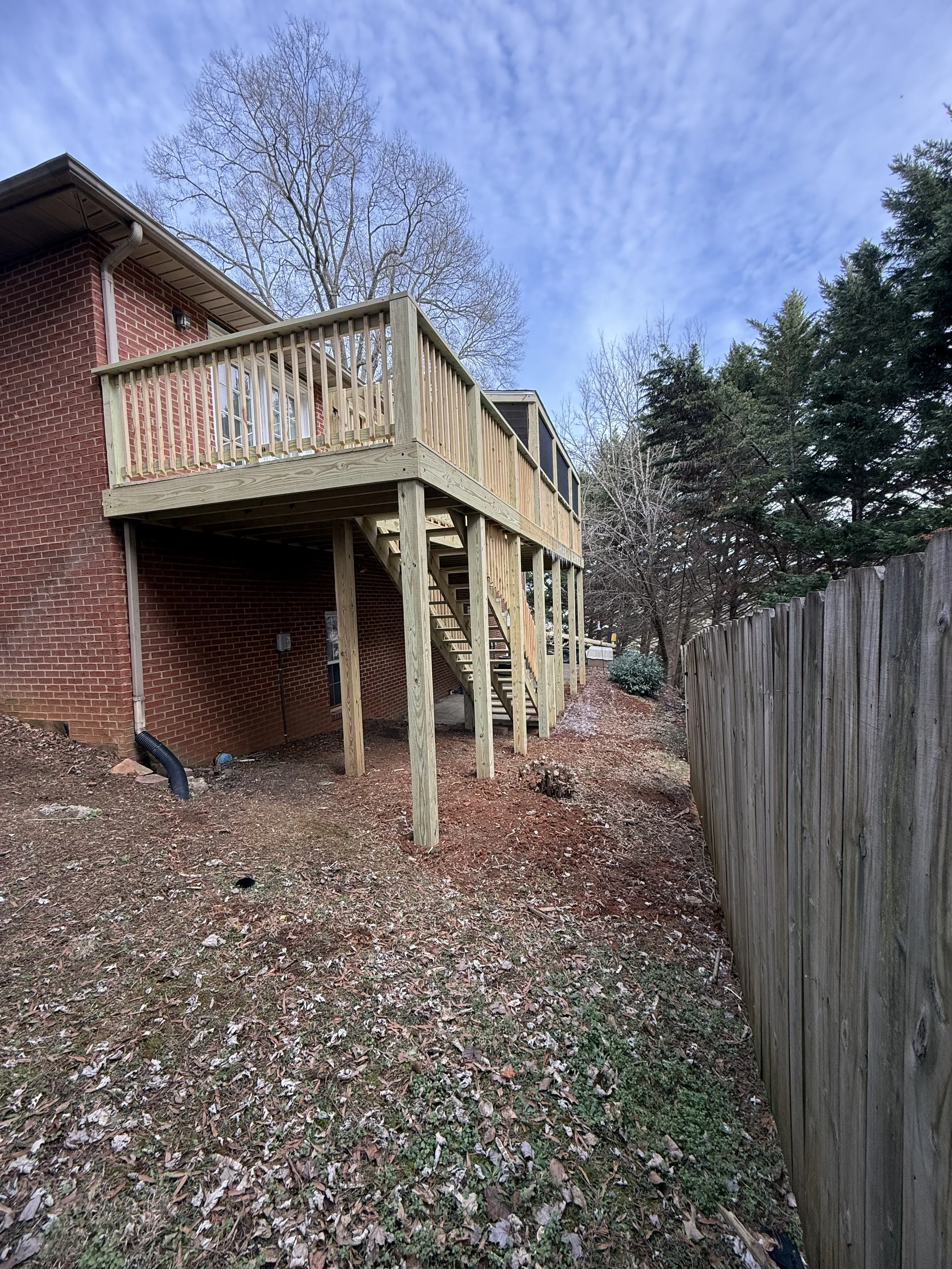 Newly constructed wooden deck with stairs, attached to a brick house, in a backyard with fallen leaves and a wooden fence on the right in Maryville, TN