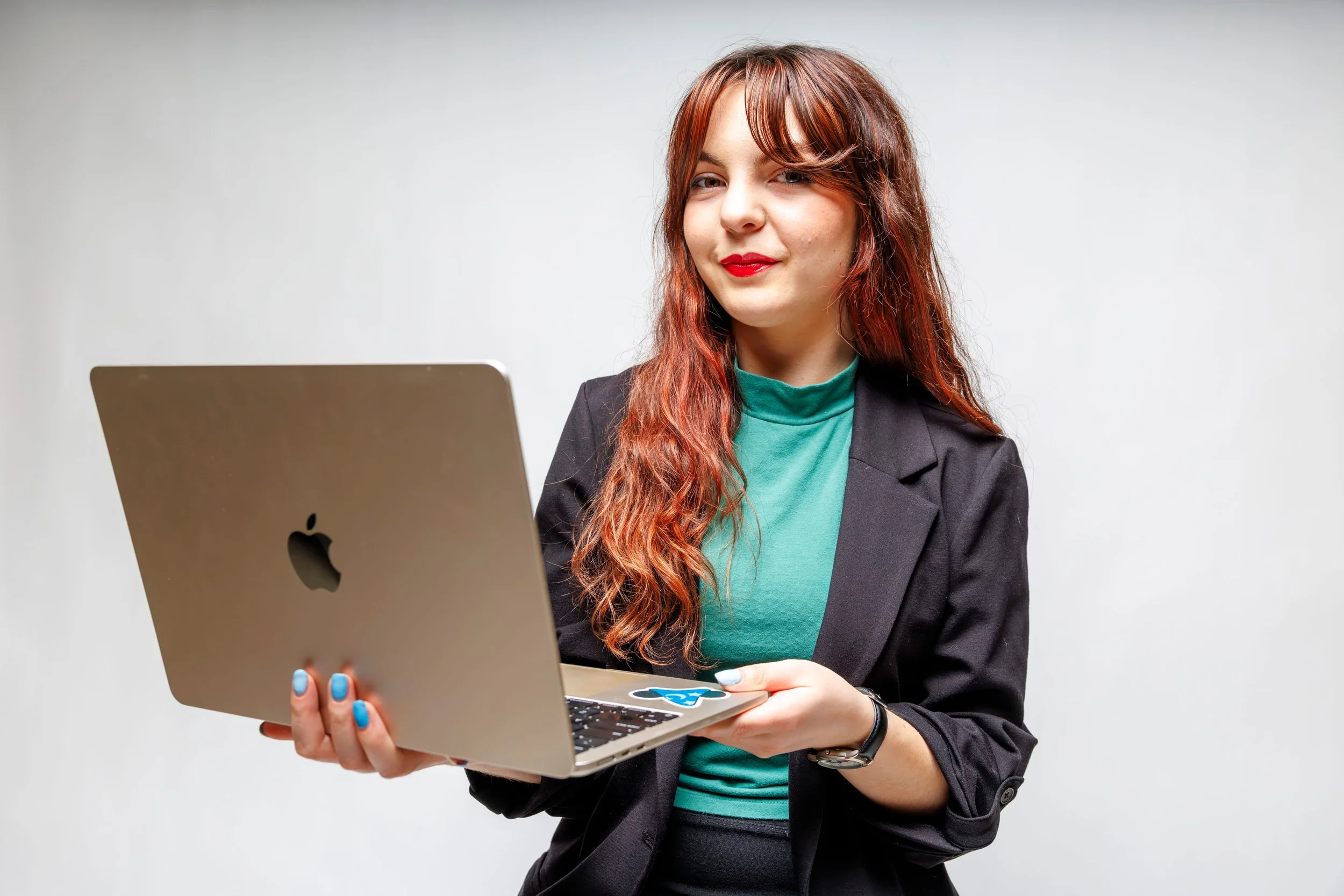 Chelsea, in professional dress, holds her MacBook while smiling at the camera.