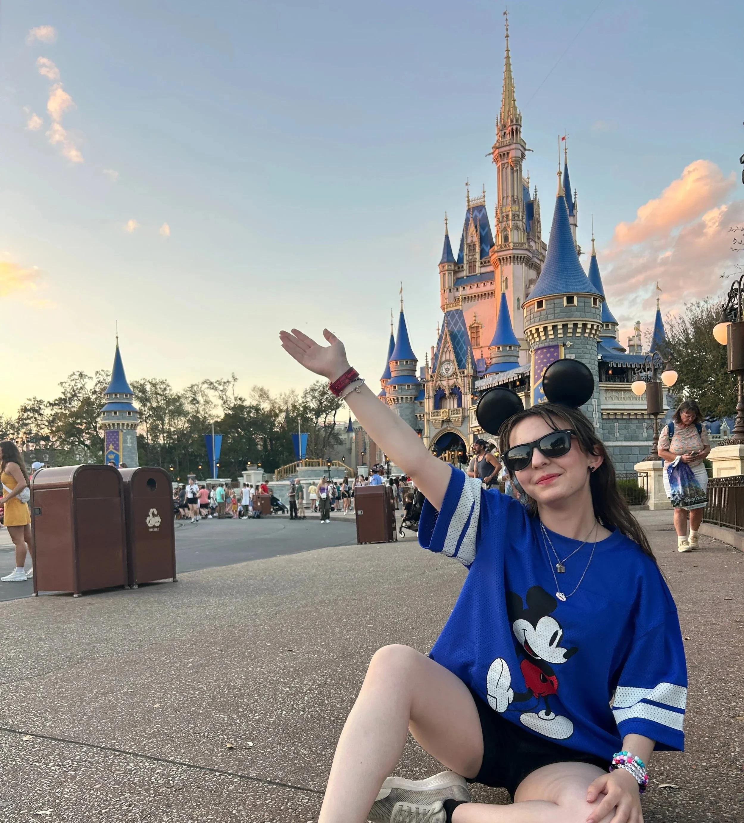 Chelsea is sitting in front of Cinderella Castle with her hand in the air.