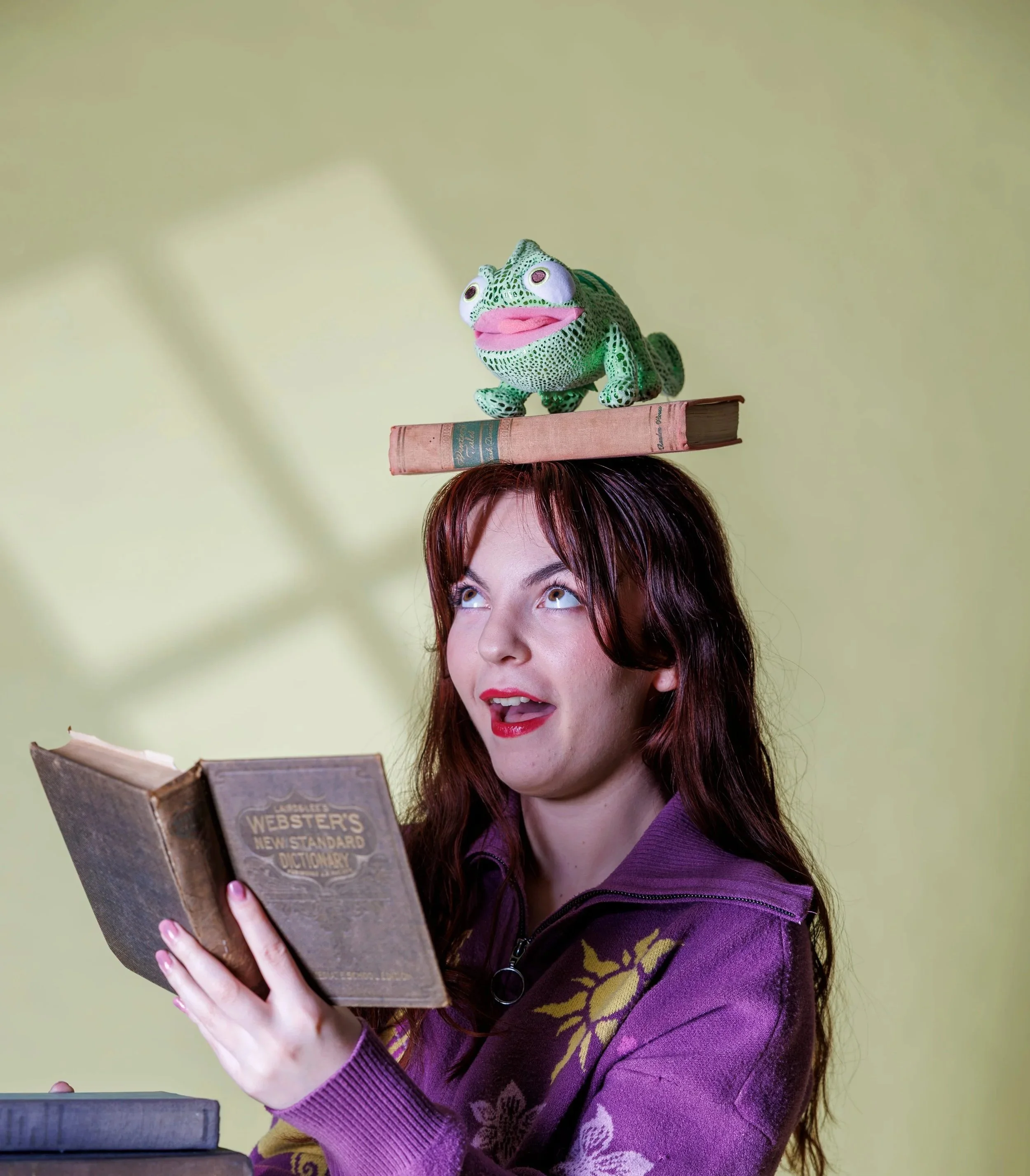 Chelsea poses holding a book in her hand with another balanced on top of her head with a stuffed animal Pasqual. 