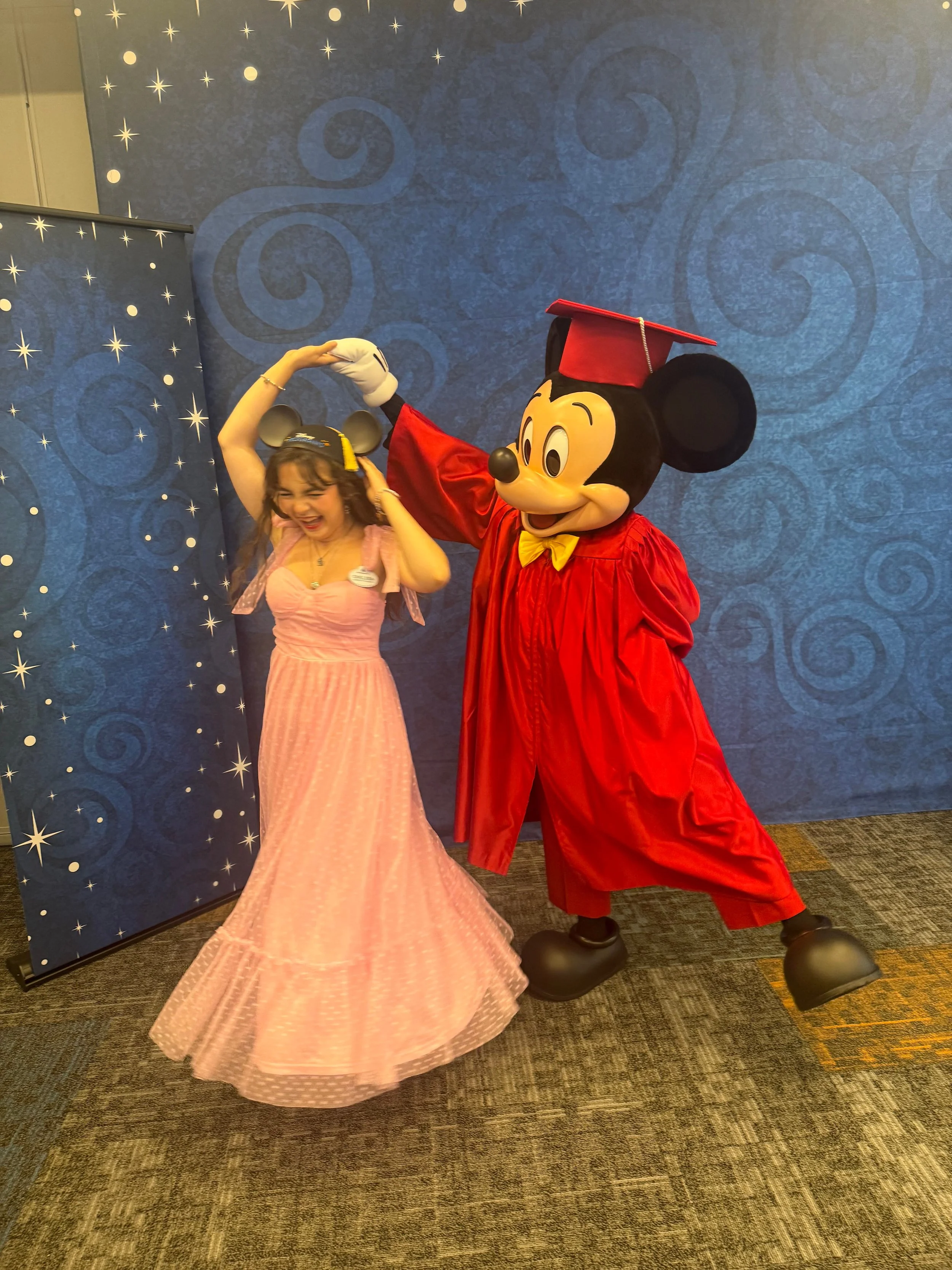 Chelsea twirls with Mickey Mouse in a graduation gown at her Disney College Program graduation.