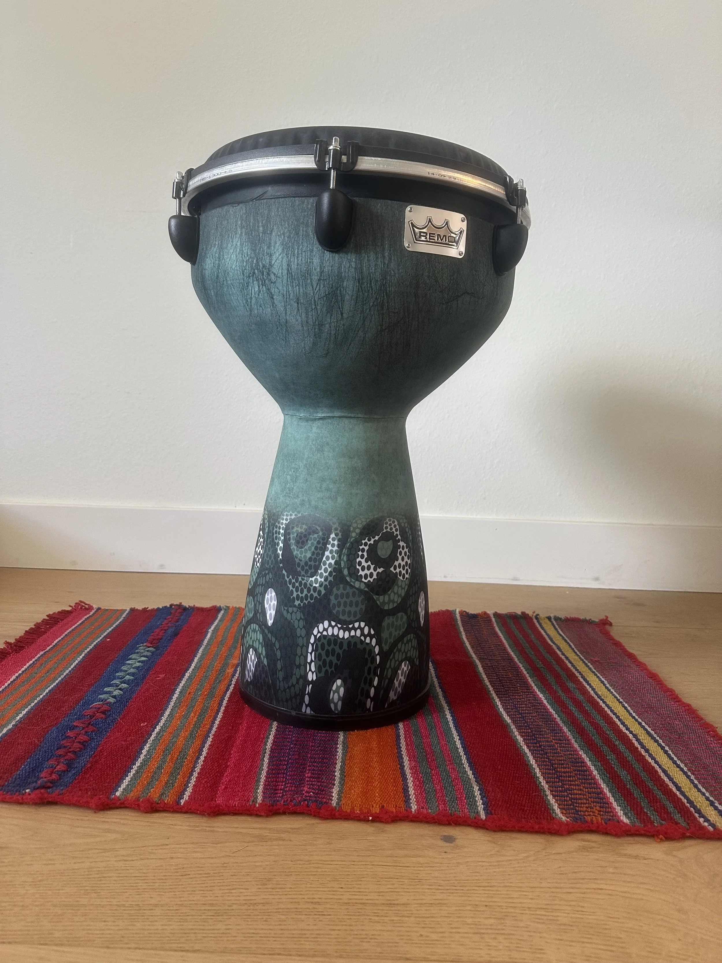 A drum on a colorful striped rug placed on a wooden floor against a plain wall.