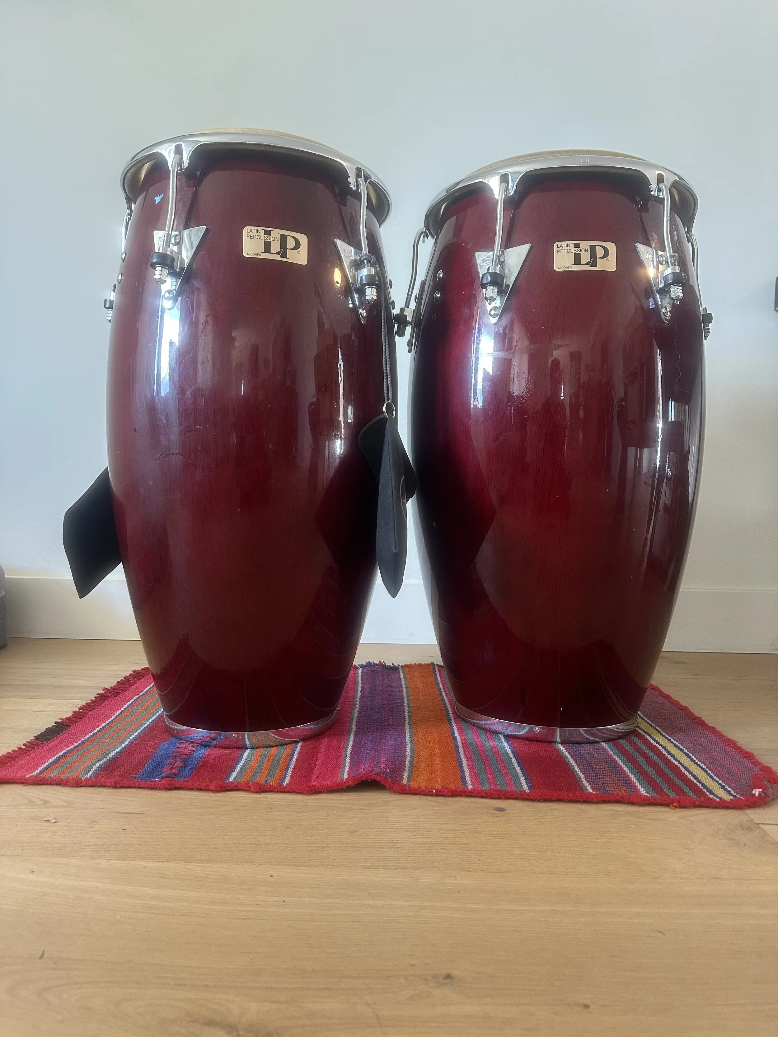 Pair of maroon conga drums on a colorful striped rug.