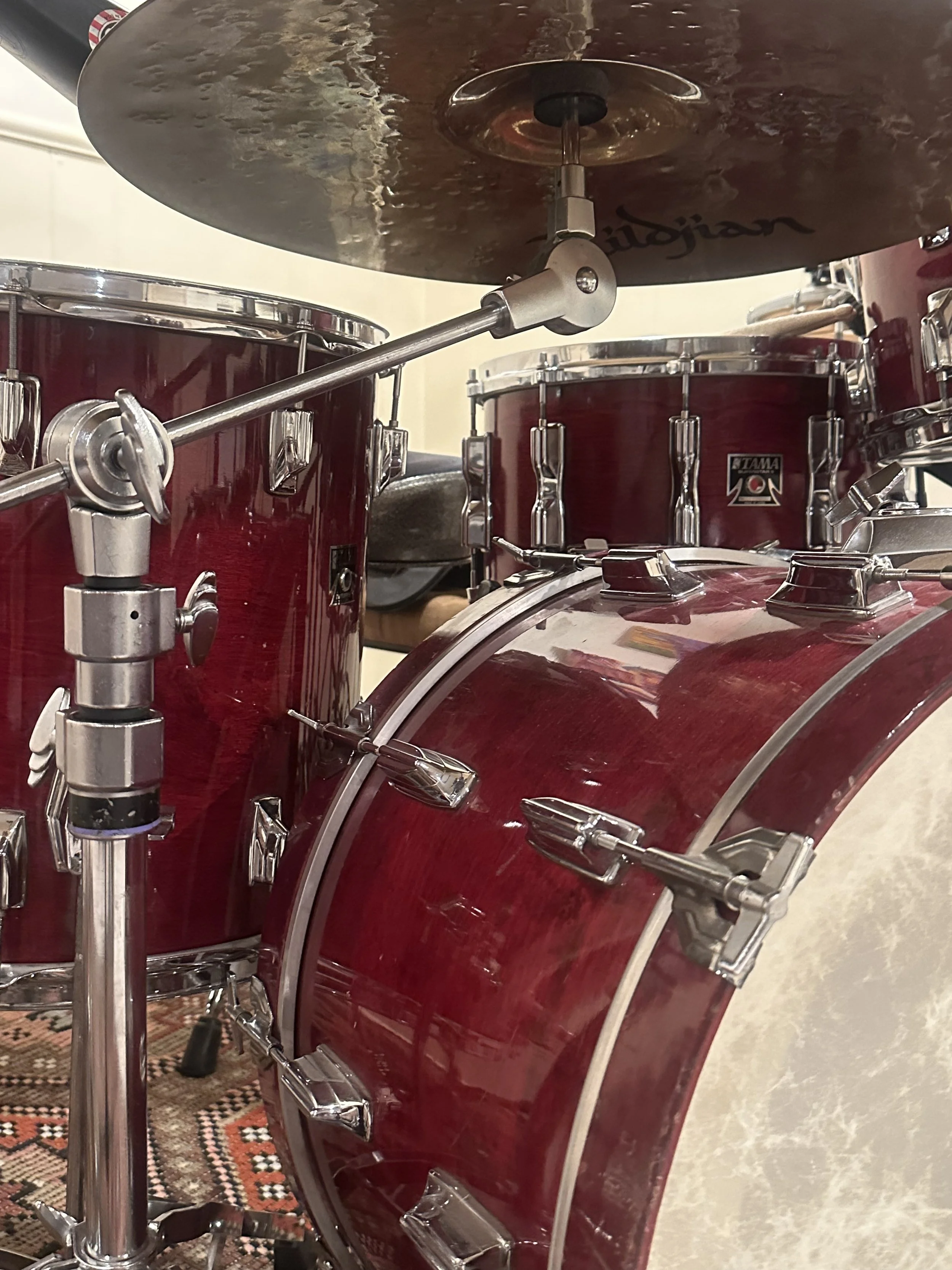 Close-up of a red drum set with a cymbal mounted above it, set on a patterned rug.