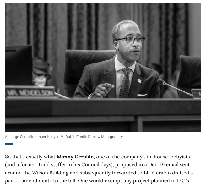Black and white photo of Kenyan McDuffie, a council member, seated at a desk during a meeting, wearing a suit and glasses, with a microphone in front of him.