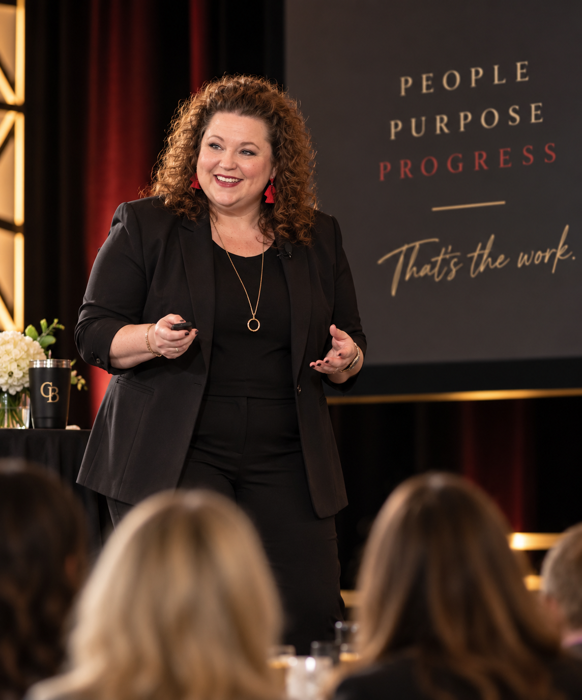Woman giving a presentation at a conference about purpose and progress with an audience watching.