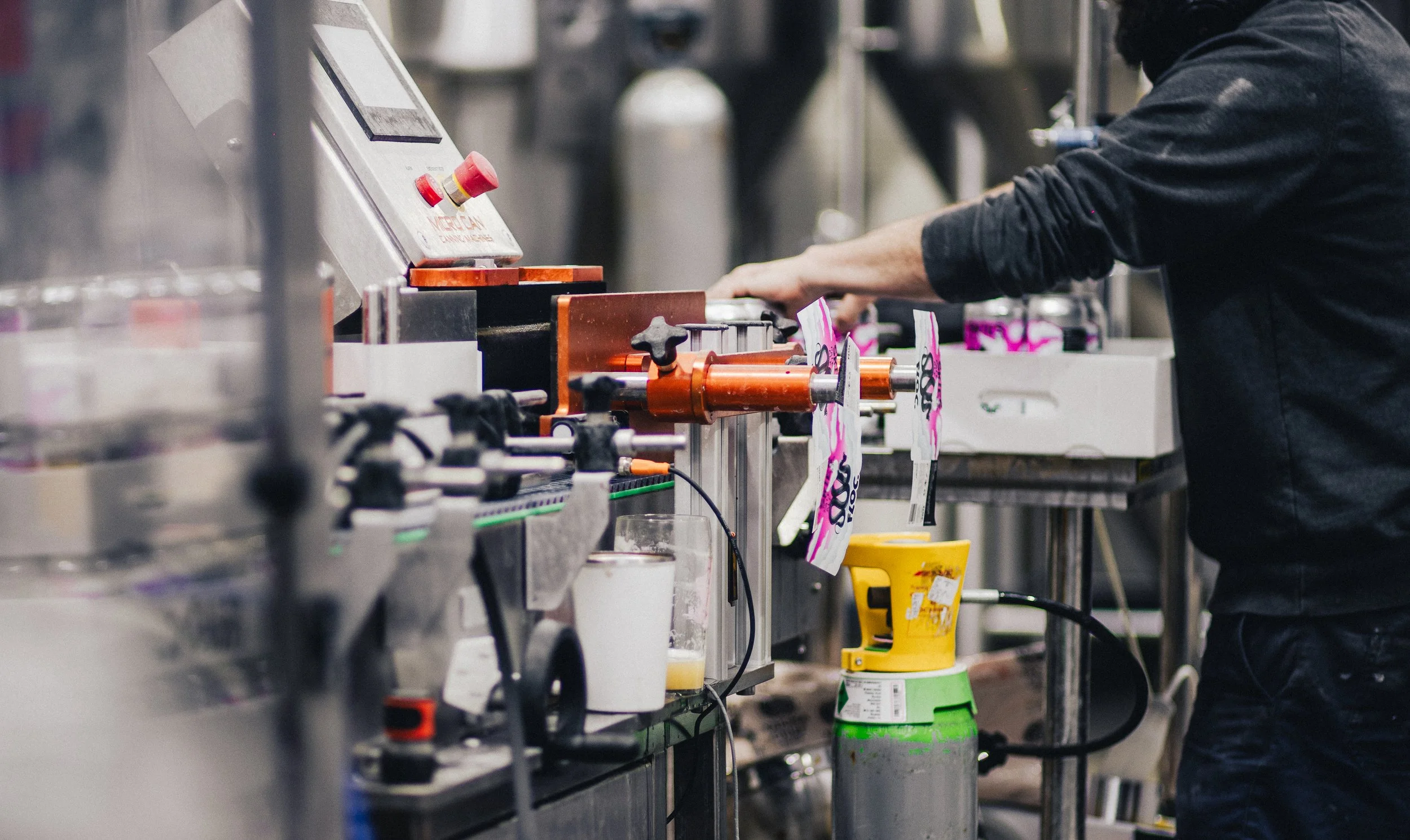 A person in black clothing operating industrial equipment in a factory or workshop setting, with various tools and machinery visible.