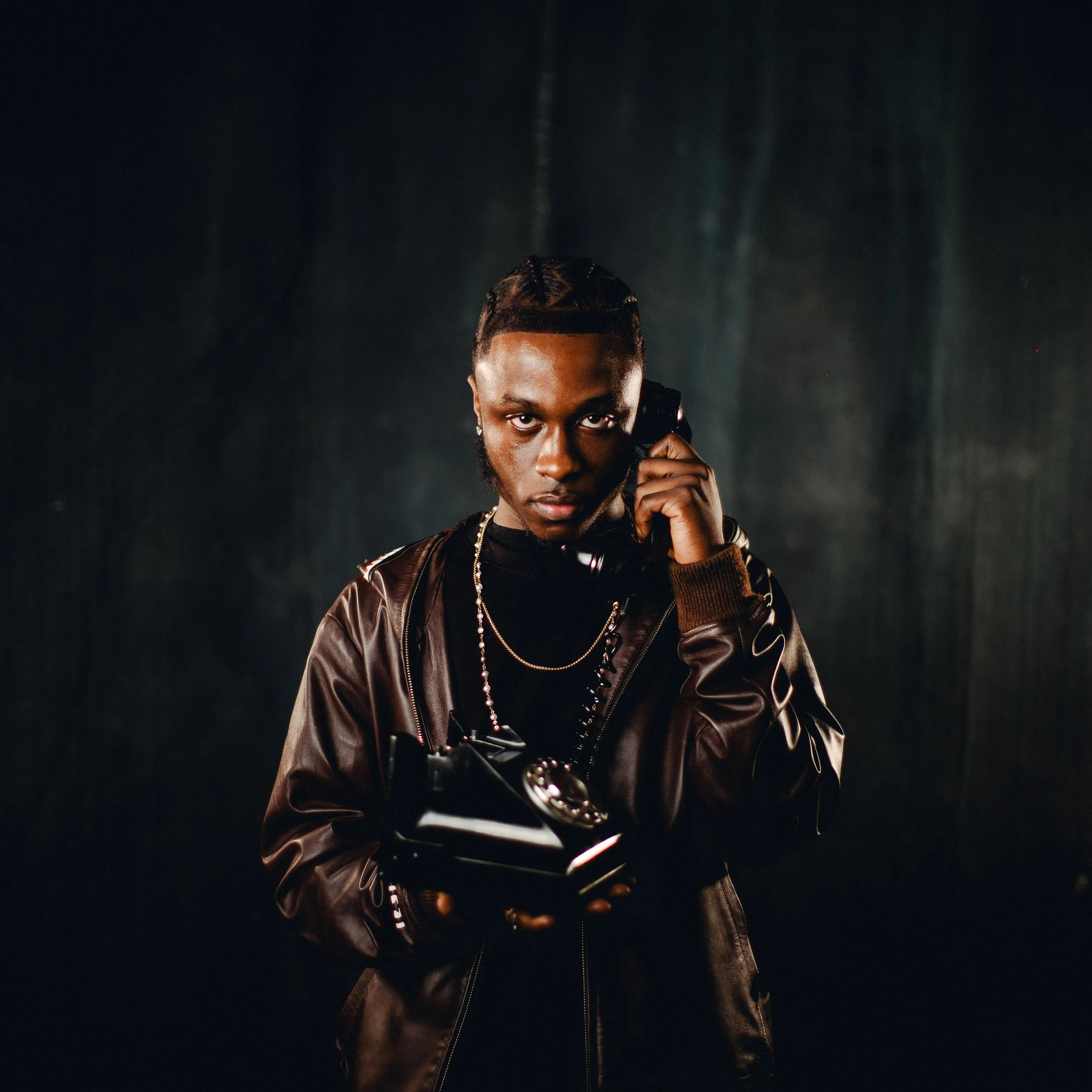 Man in a leather jacket holding a vintage telephone and talking on the phone, with a dark background.