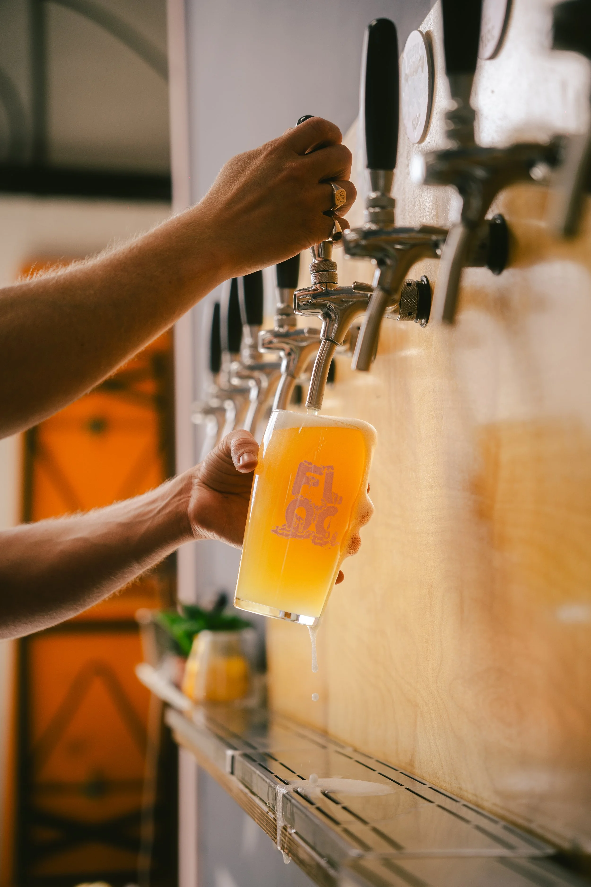A person is filling a glass of beer from a tap. The glass is being held at an angle, and beer is overflowing as it is poured.