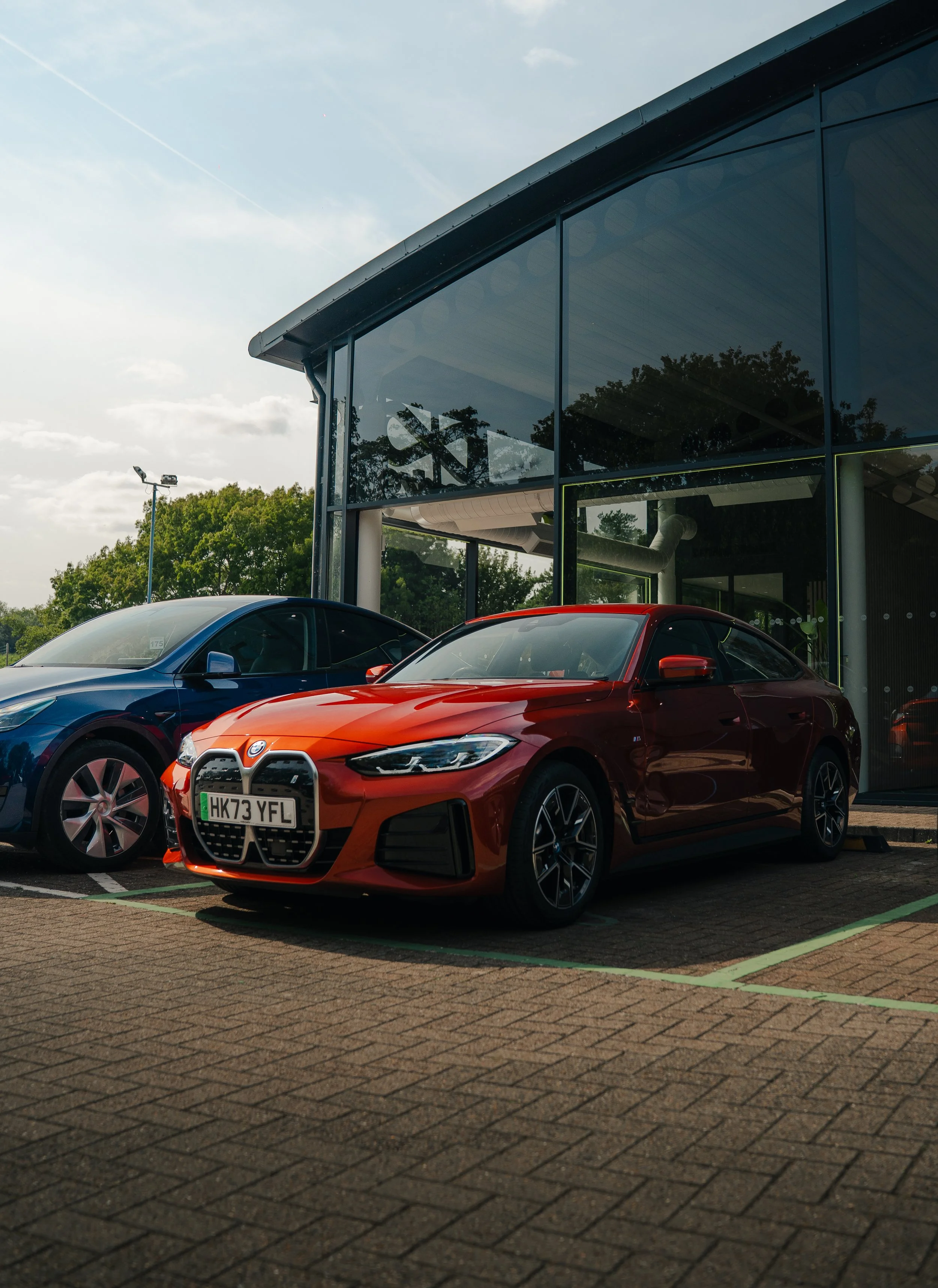Red sports car parked next to a black car outside a modern building with glass walls.