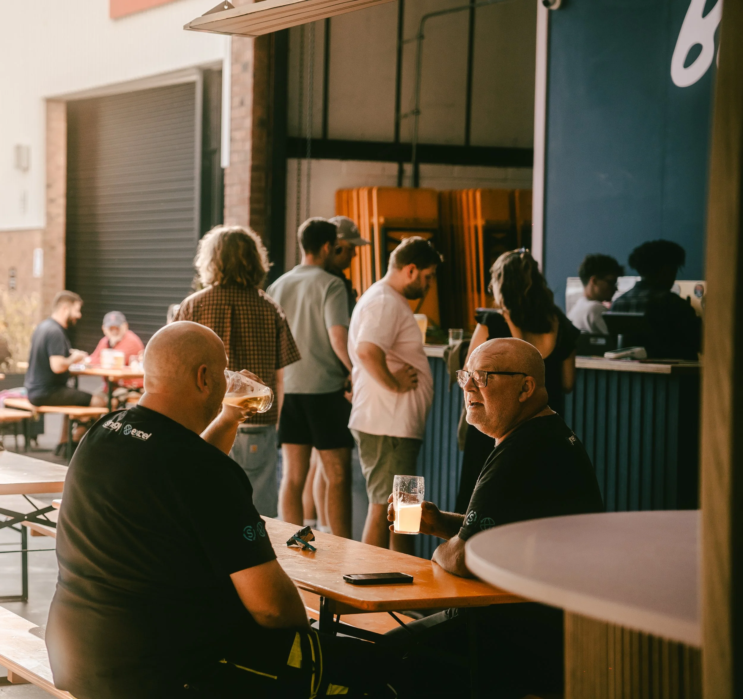 People socializing and ordering drinks at an outdoor bar in the evening, with some seated and others standing in line.