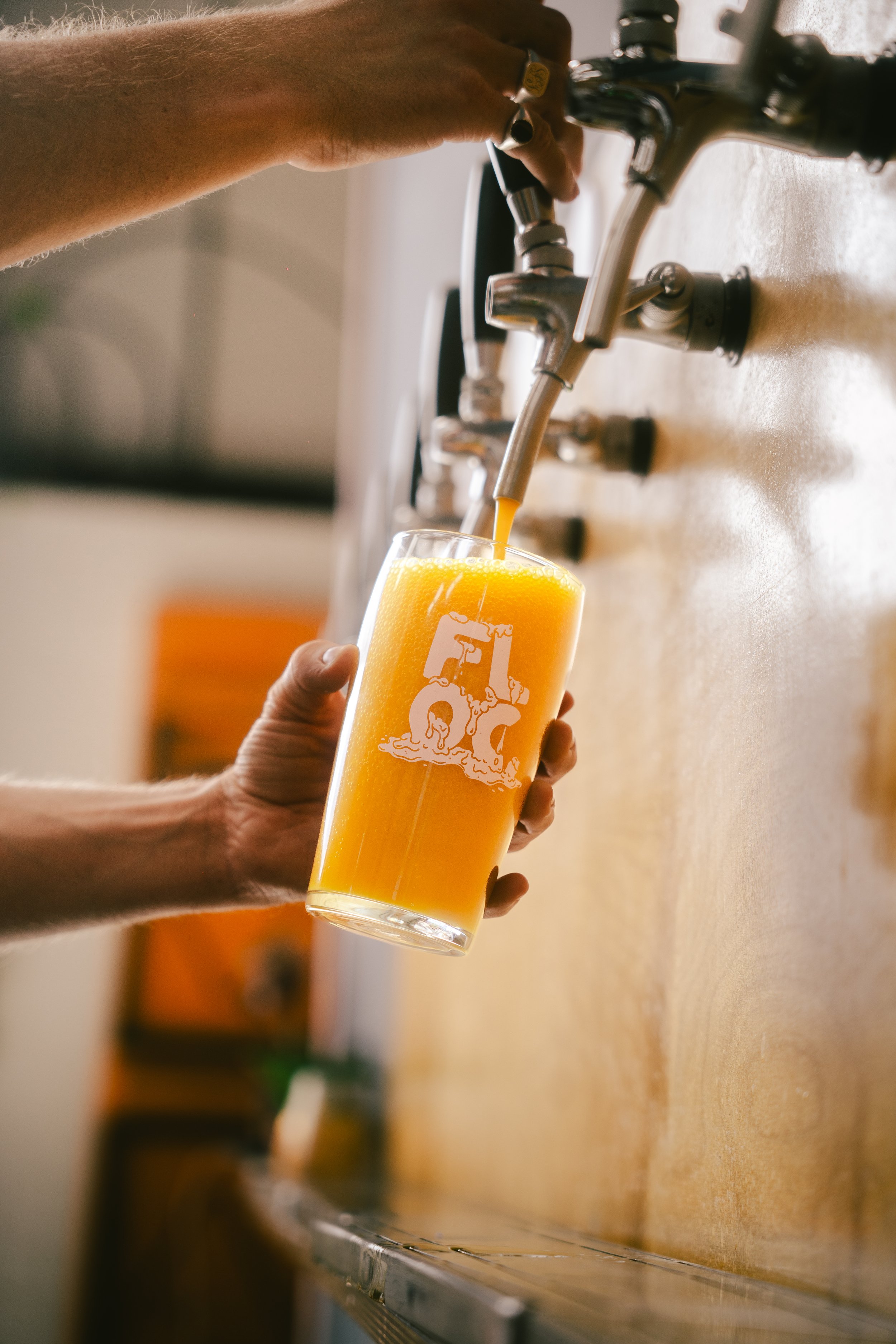 Person pouring orange juice from a tap into a glass with a logo on it.