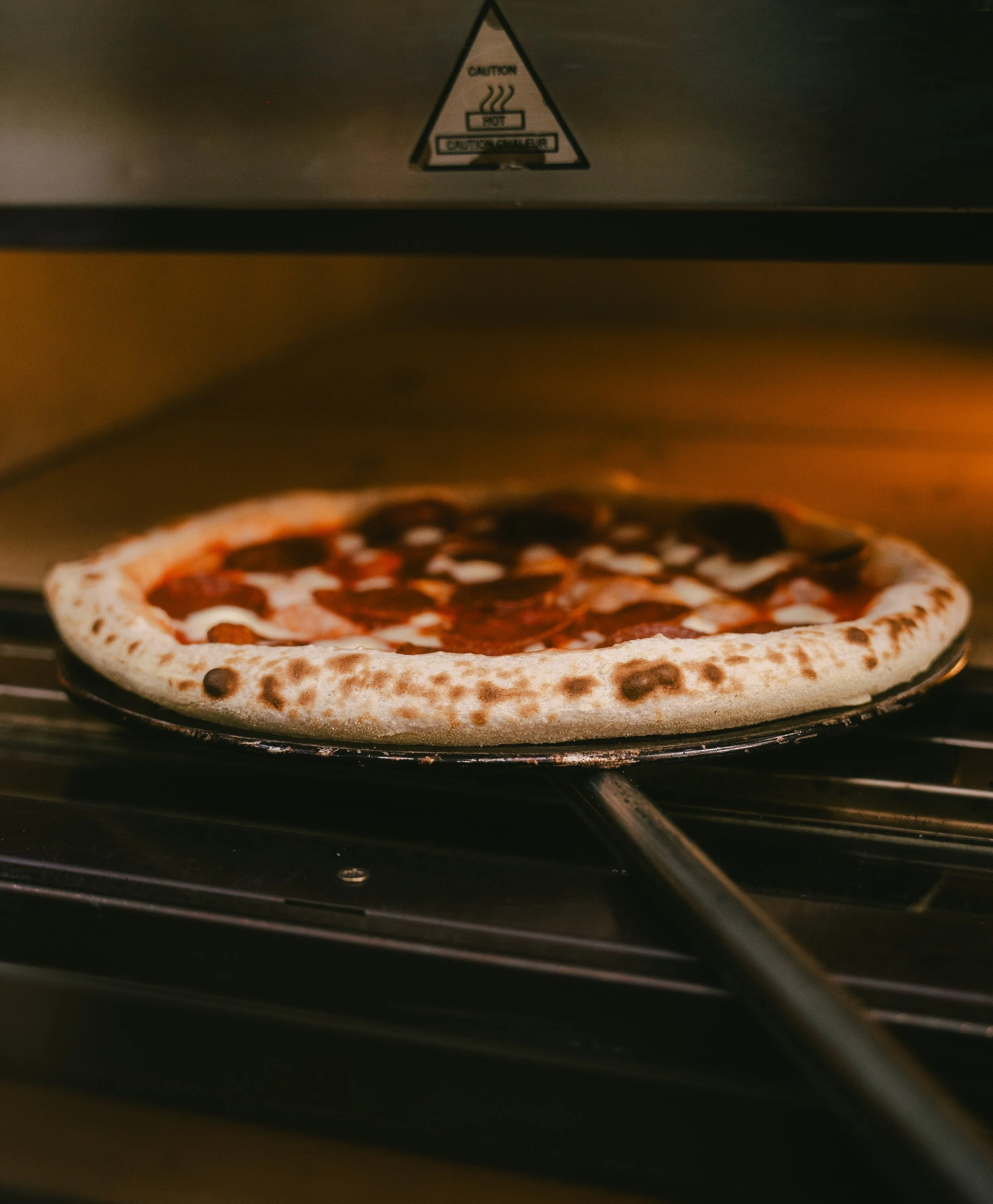 Pizza baking inside an oven with a caution label on the oven door.