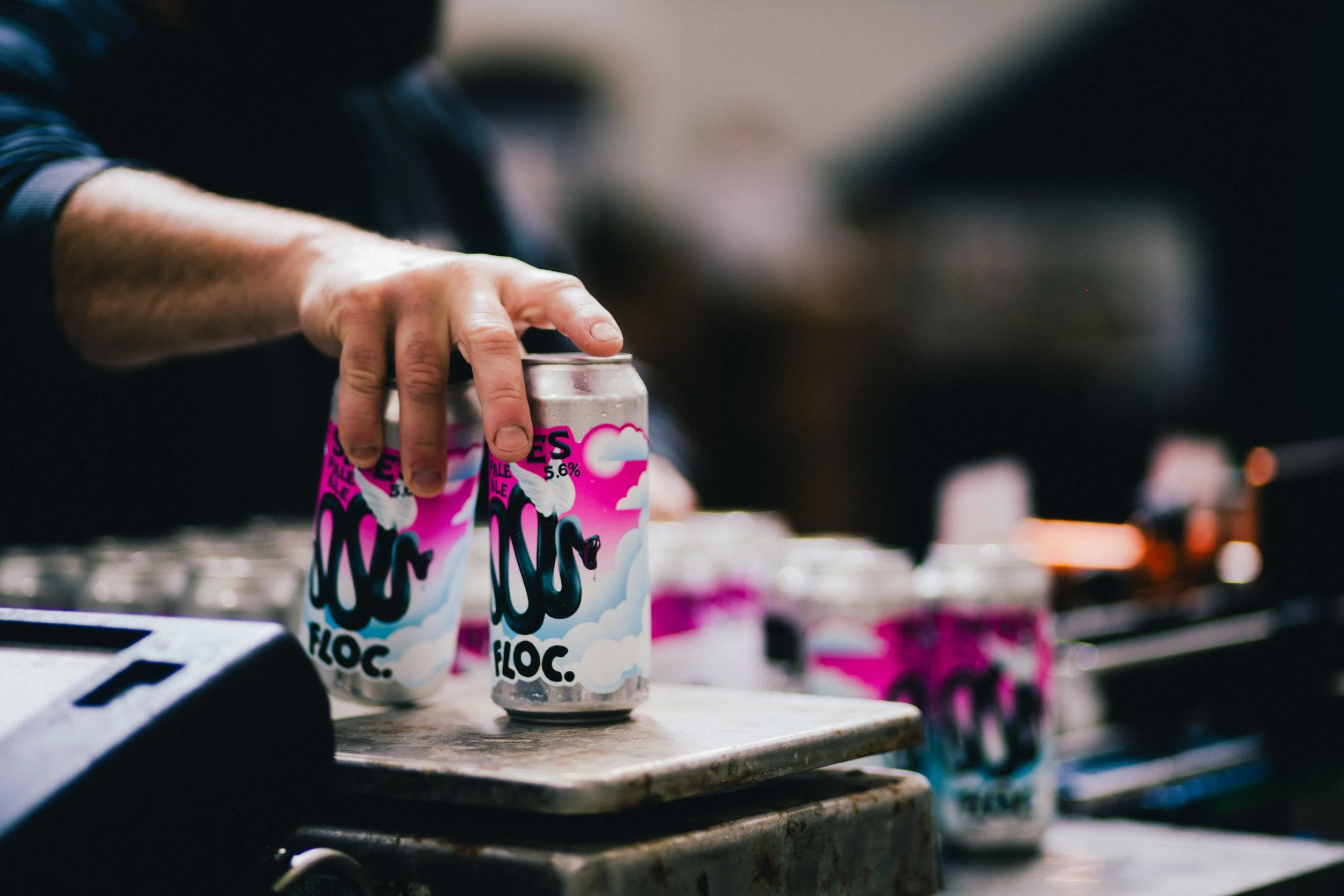 A person with a black shirt is placing a can of Bubble F loc beer on a table, with more cans of the same brand visible in the background.