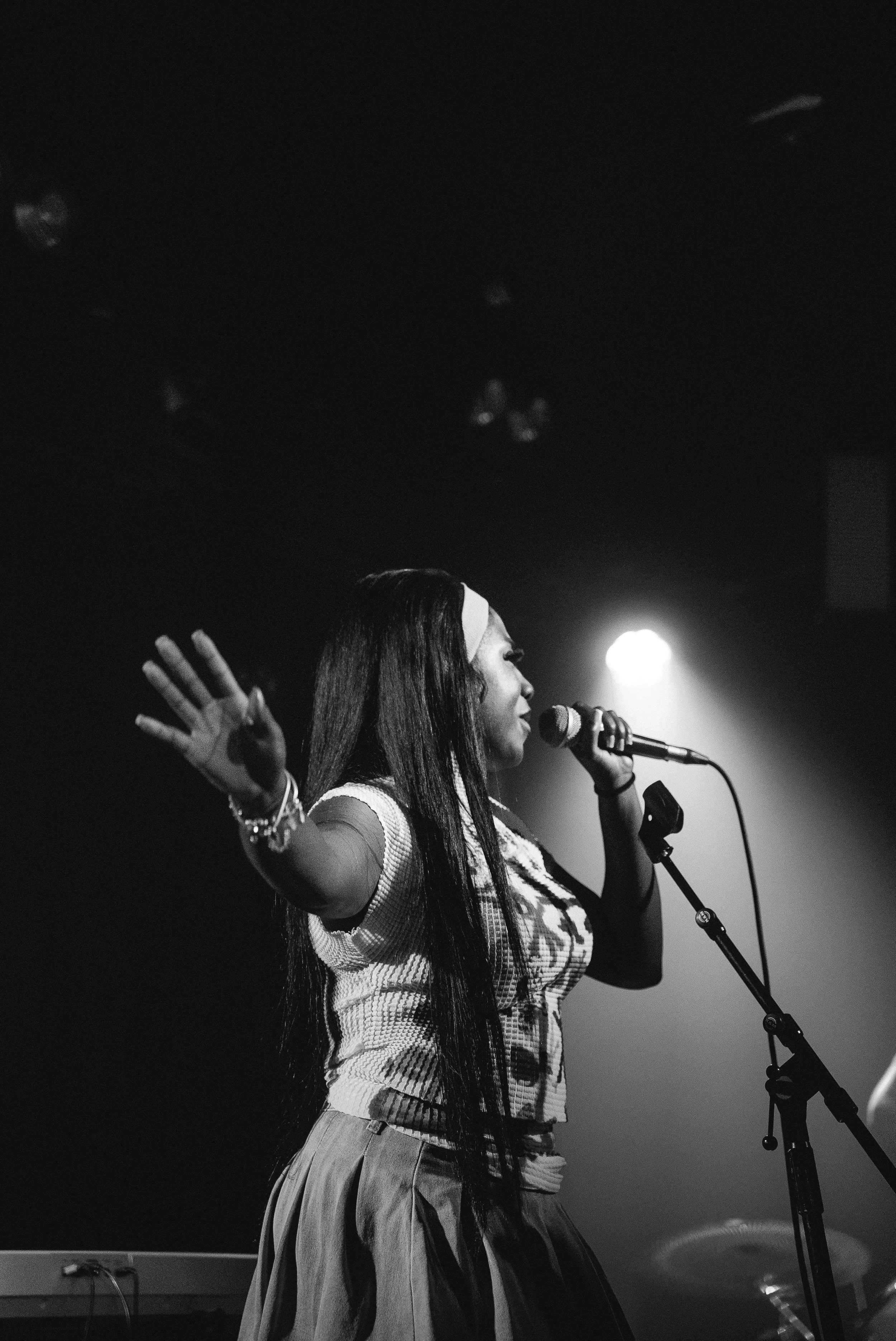 A black-and-white photo of a woman singing into a microphone on stage, with her eyes closed and one arm raised.