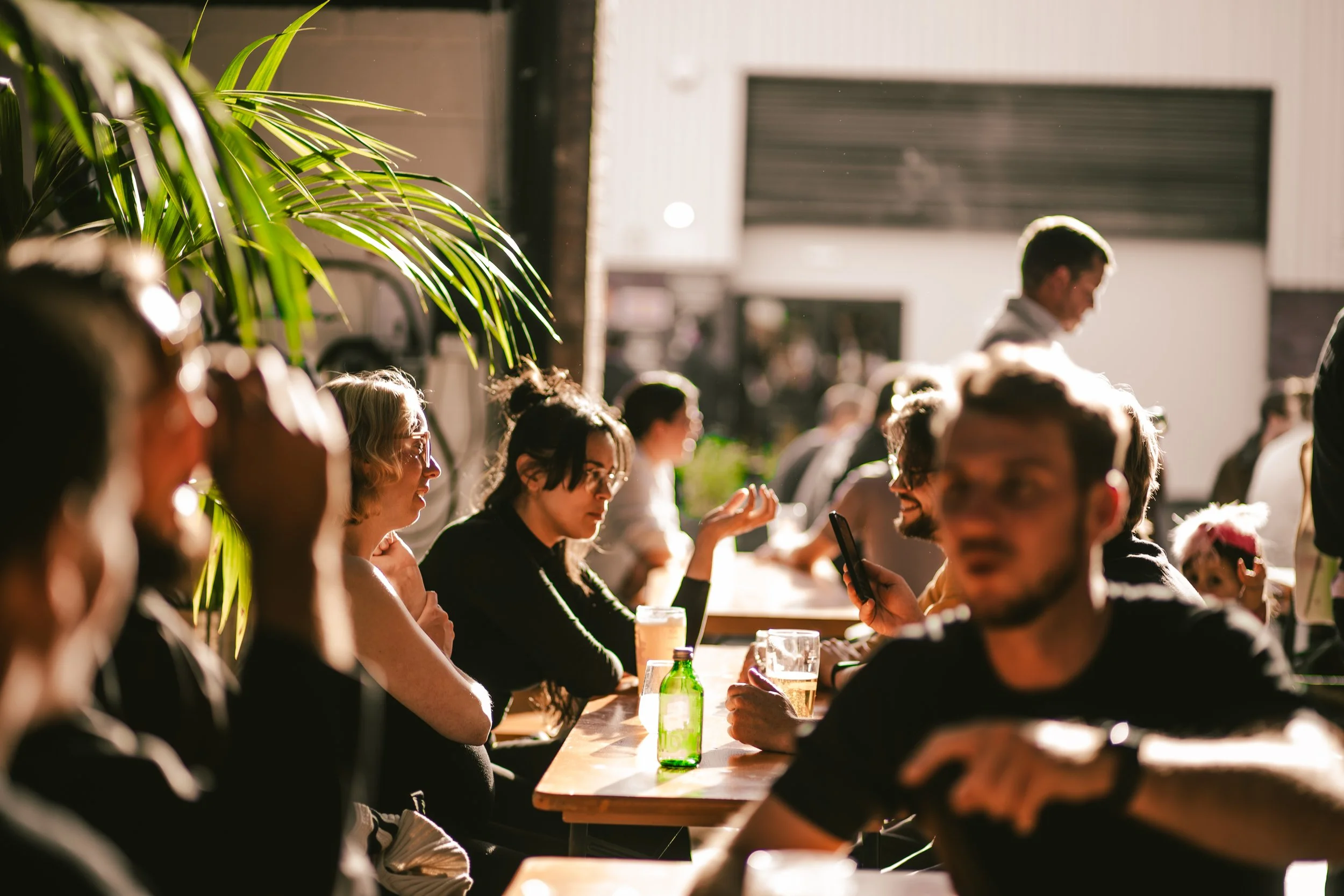 People sitting outdoors at a sunny patio, drinking beverages and chatting with each other.