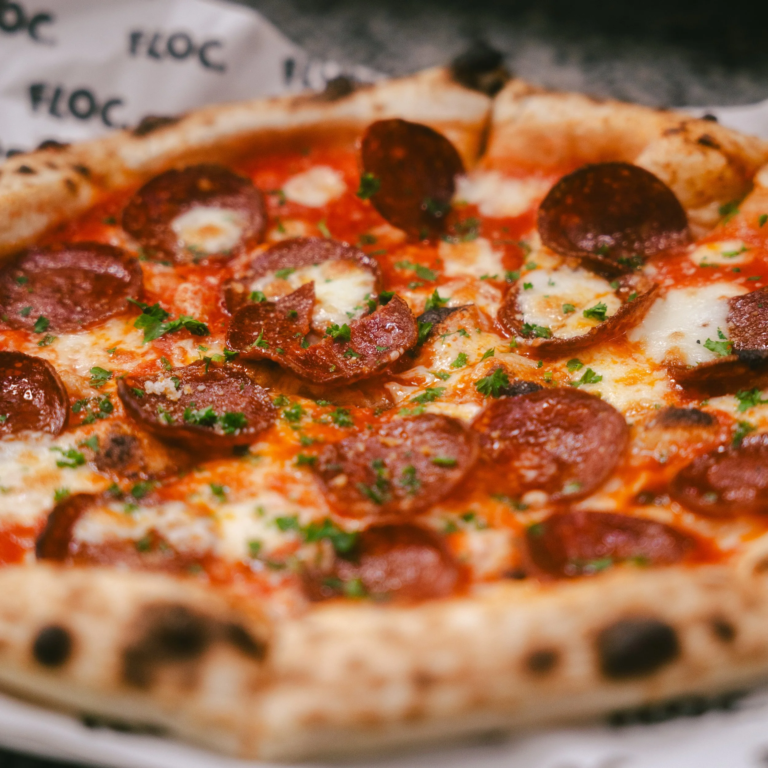 Close-up of a pepperoni pizza with melted cheese and chopped parsley on a pizza box.