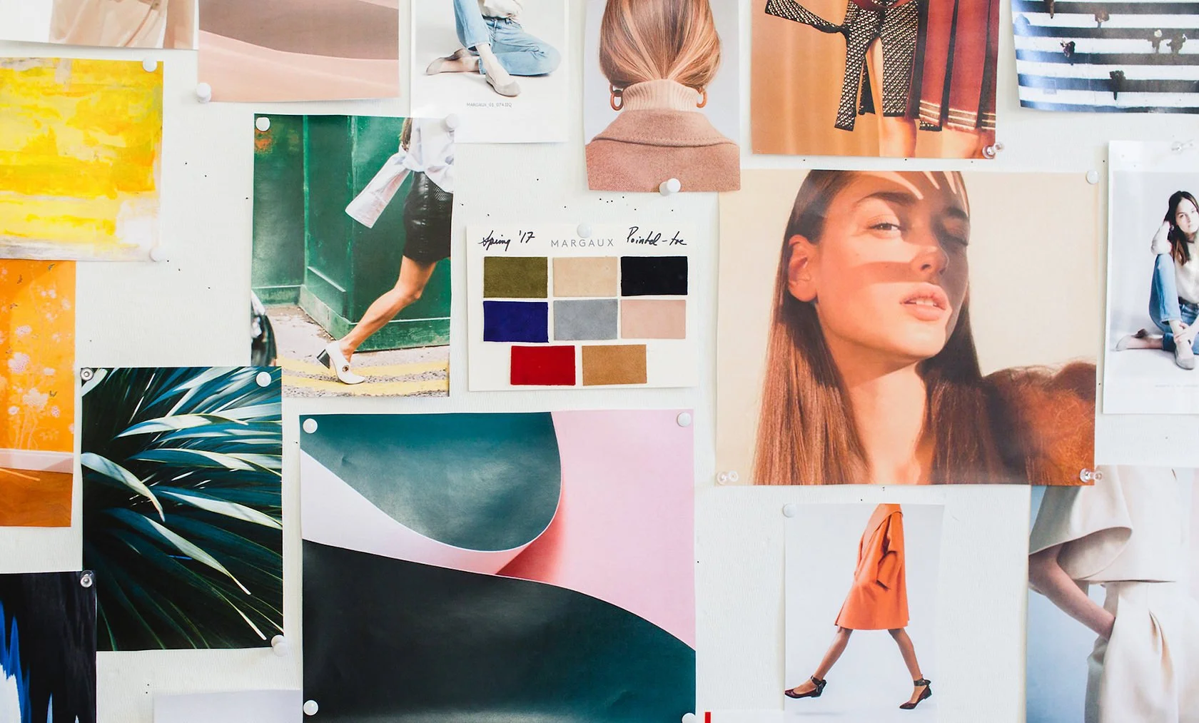 A collage of various photographs and color swatches pinned to a white wall. The images include people in fashionable poses, close-up portraits, and artistic abstract photos, along with a color swatch card labeled 'Spring '17' showing different fabric colors.