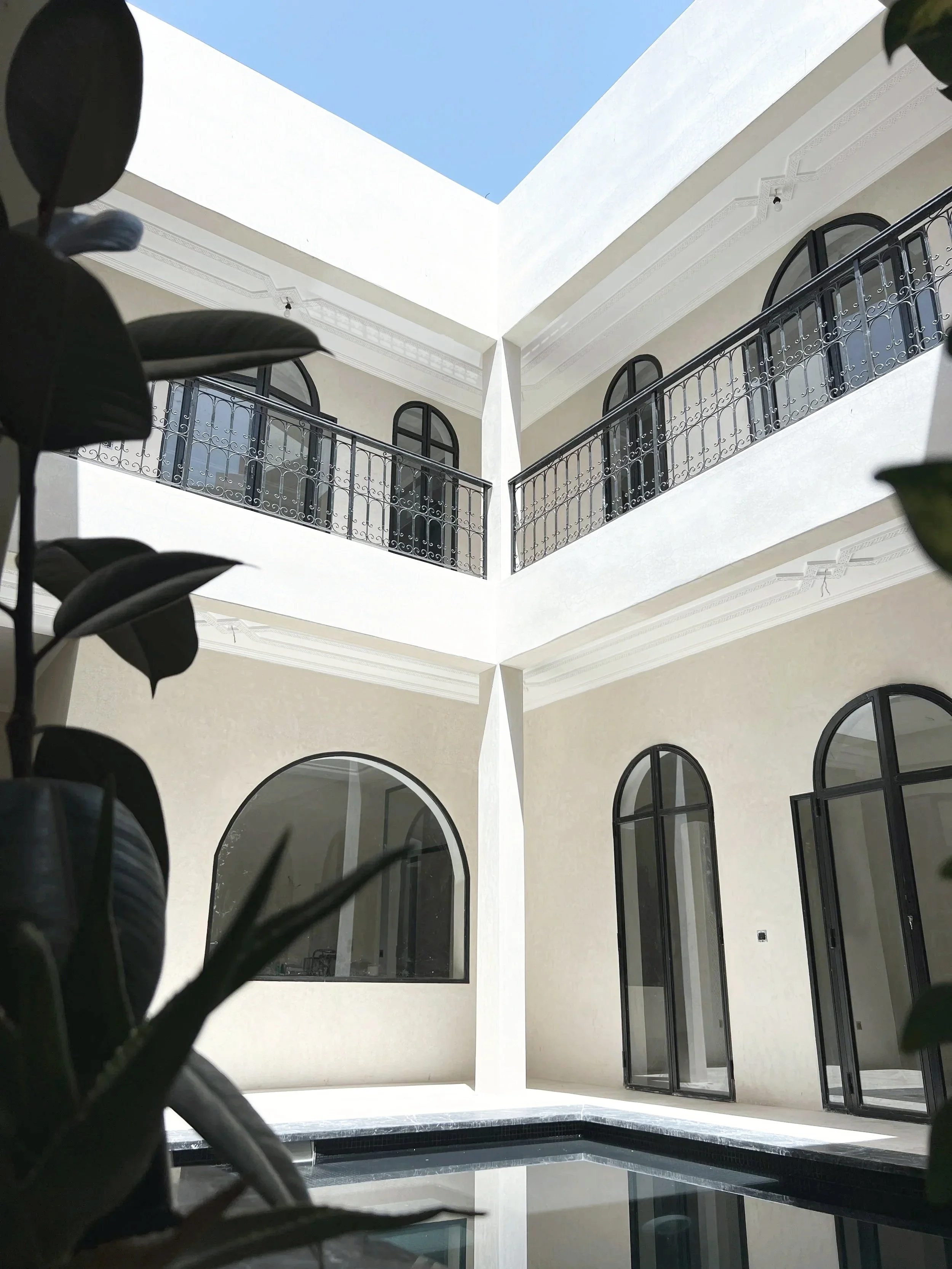 View of a modern white building with arched black-framed windows, a black wrought iron balcony railing, and an open sky overhead.