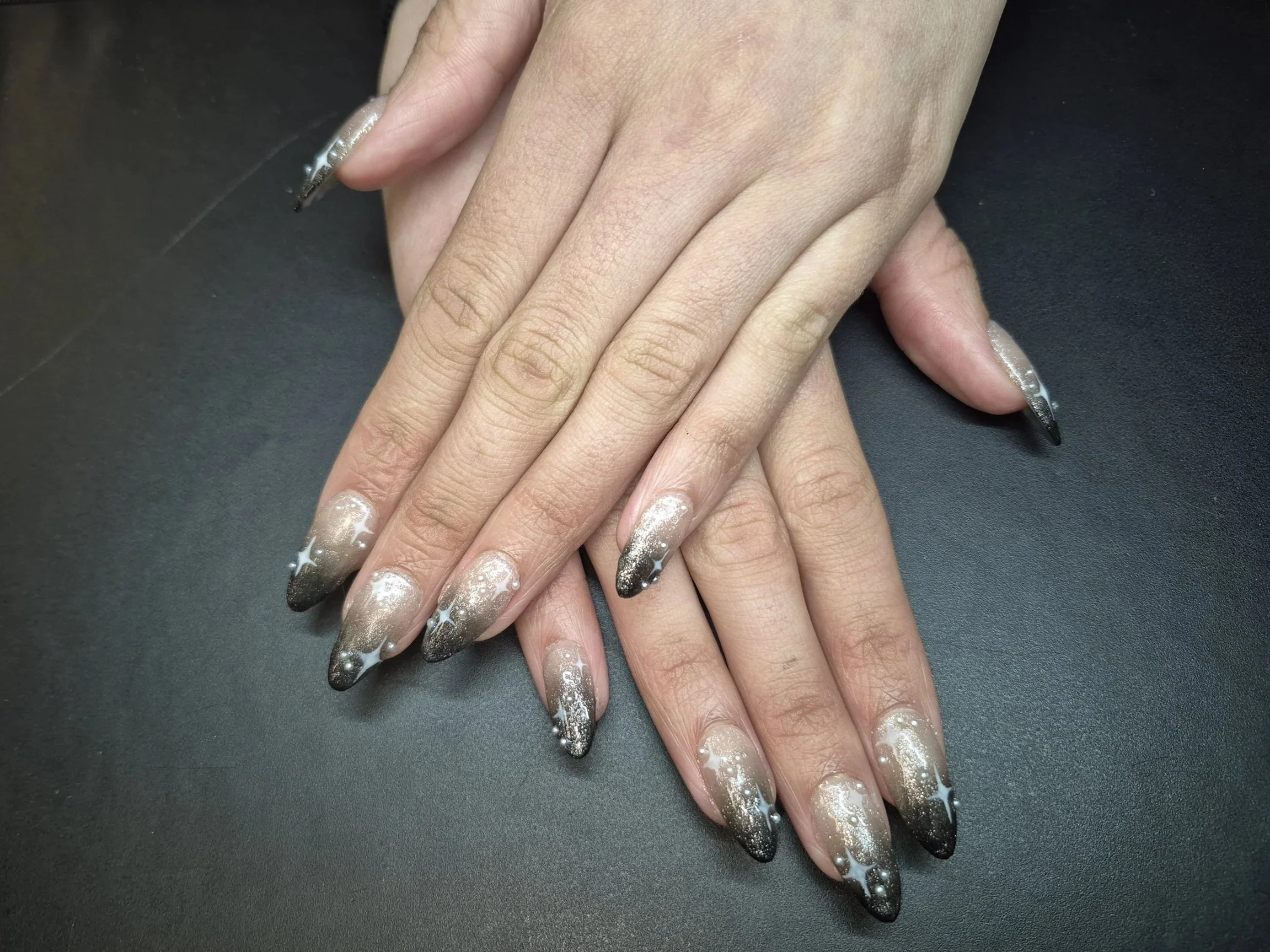 A custom set of nails for prom with a nude jelly base, black ombre, and pearl embellishments. 
