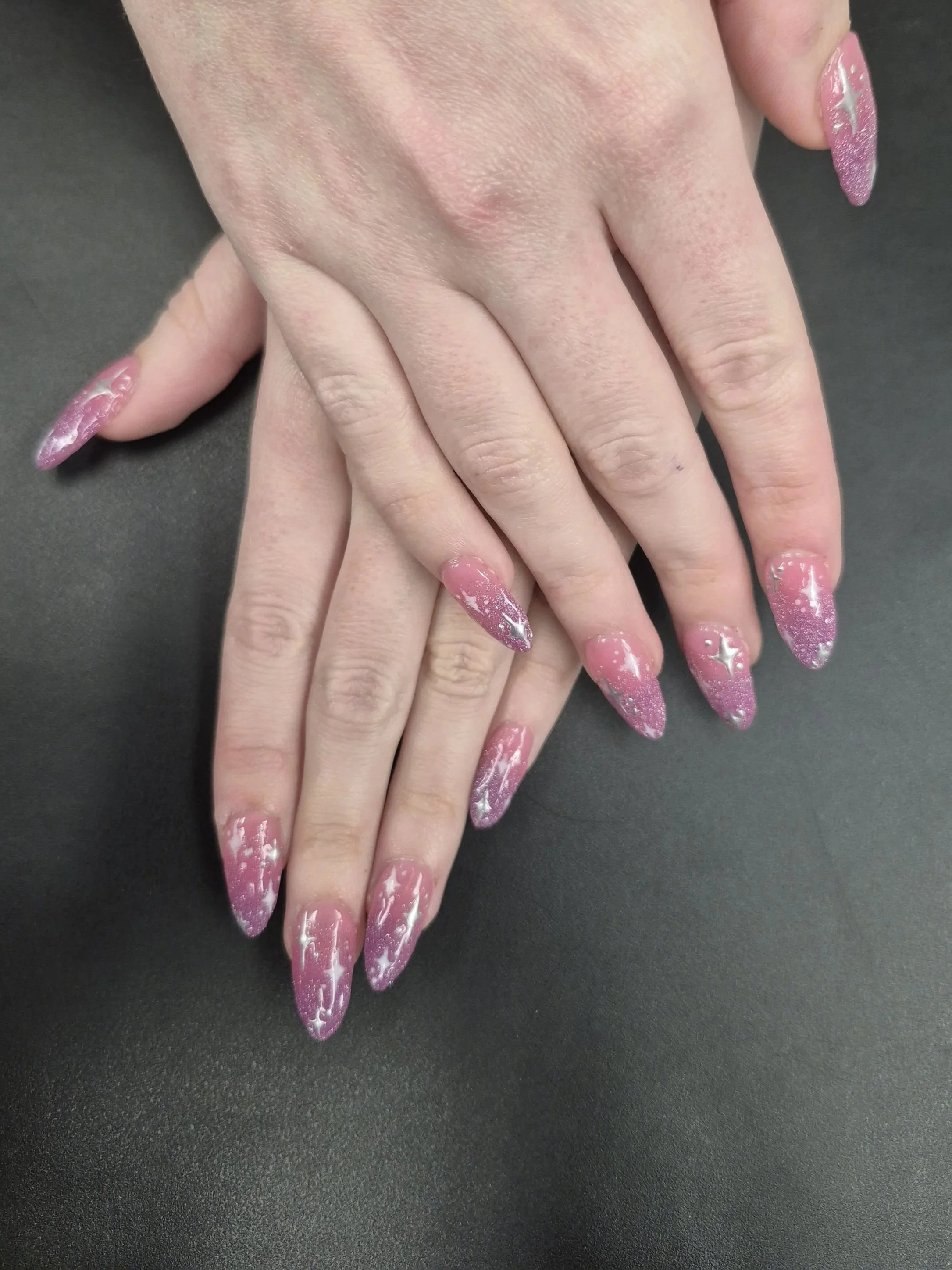 A custom set of nails with a pink jelly base and dark pink glittery ombre. Accented with white a silver chrome stars.