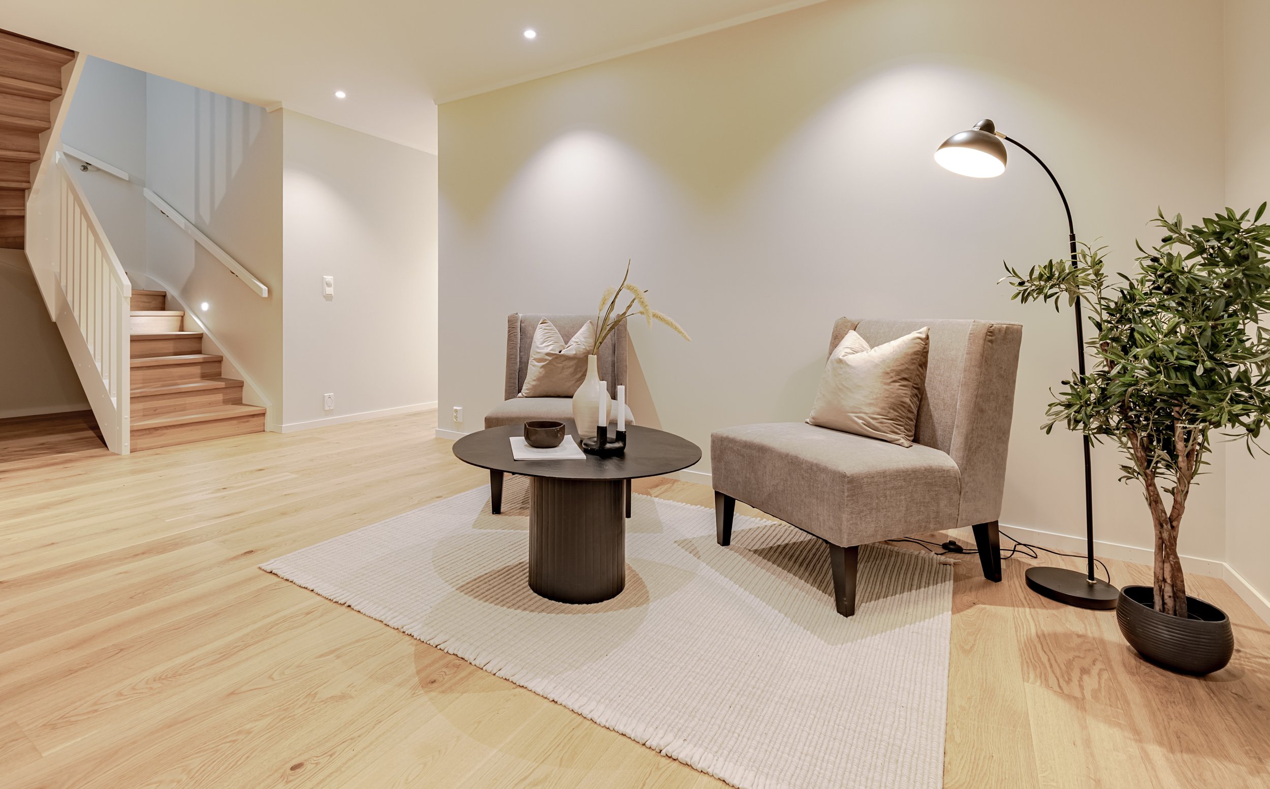 Et kjøkken med hvite skap, en kjøkkenøy med hvit benkeplate, to svarte barstoler, og himmelbelysning.