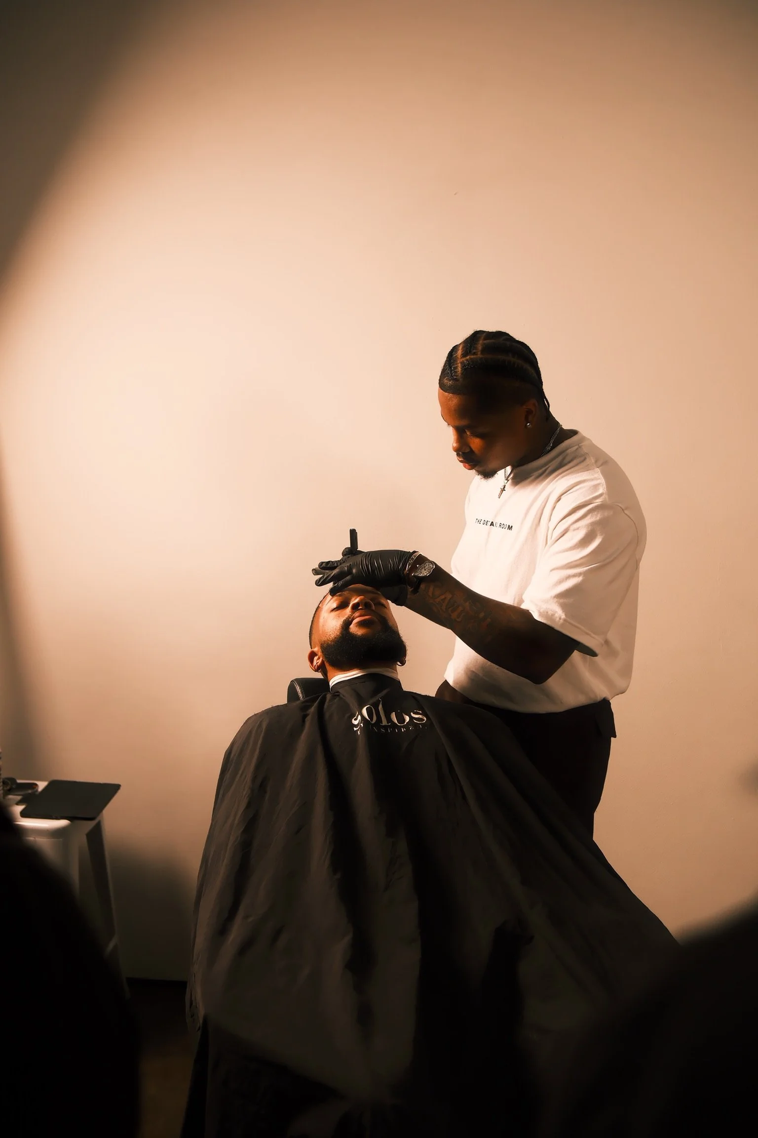Barber performing a haircut on a seated client in a salon with beige walls.