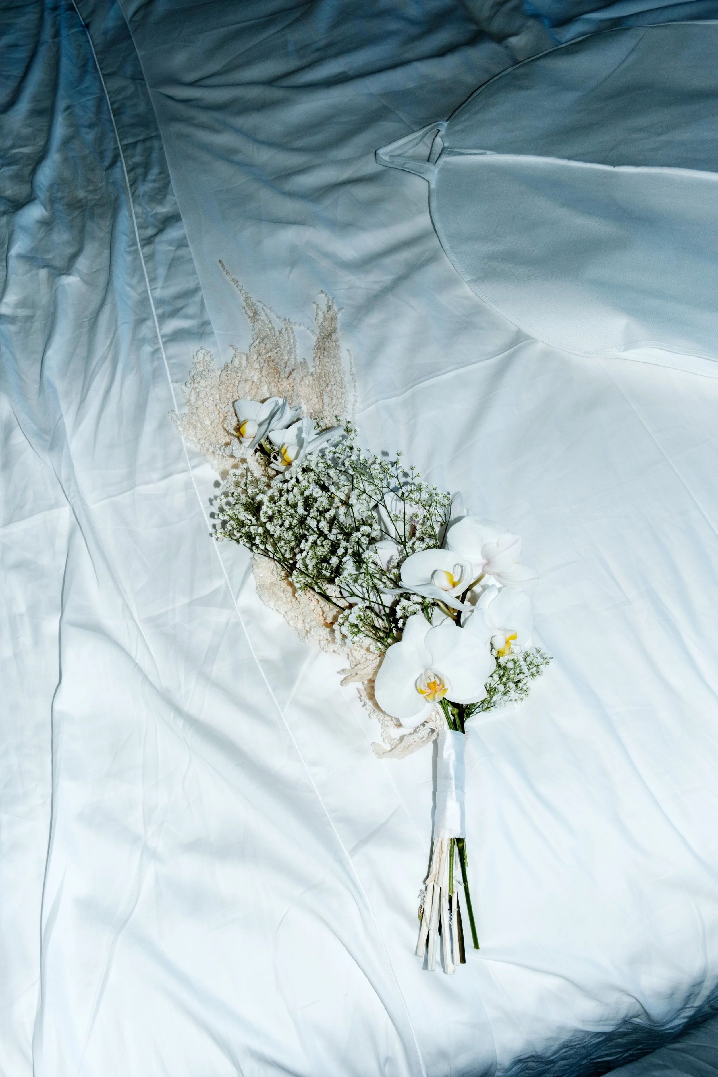 Ein Brautstrauß mit weißen Orchideen und kleinen weißen Blumen liegt auf einem weißen Stoffbett.
