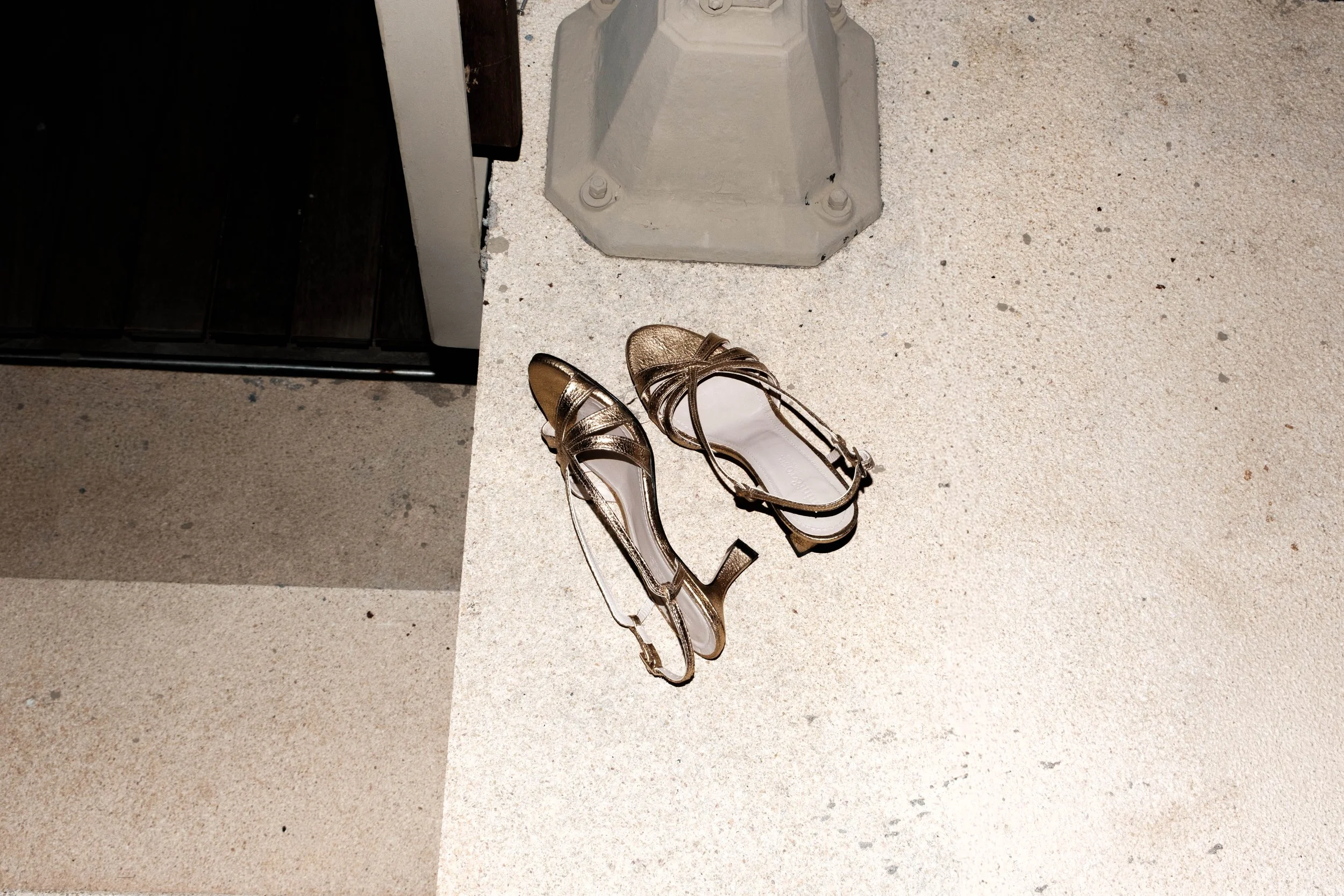 Ein Paar goldene High Heels liegen auf einem Betonboden neben einer Wand.