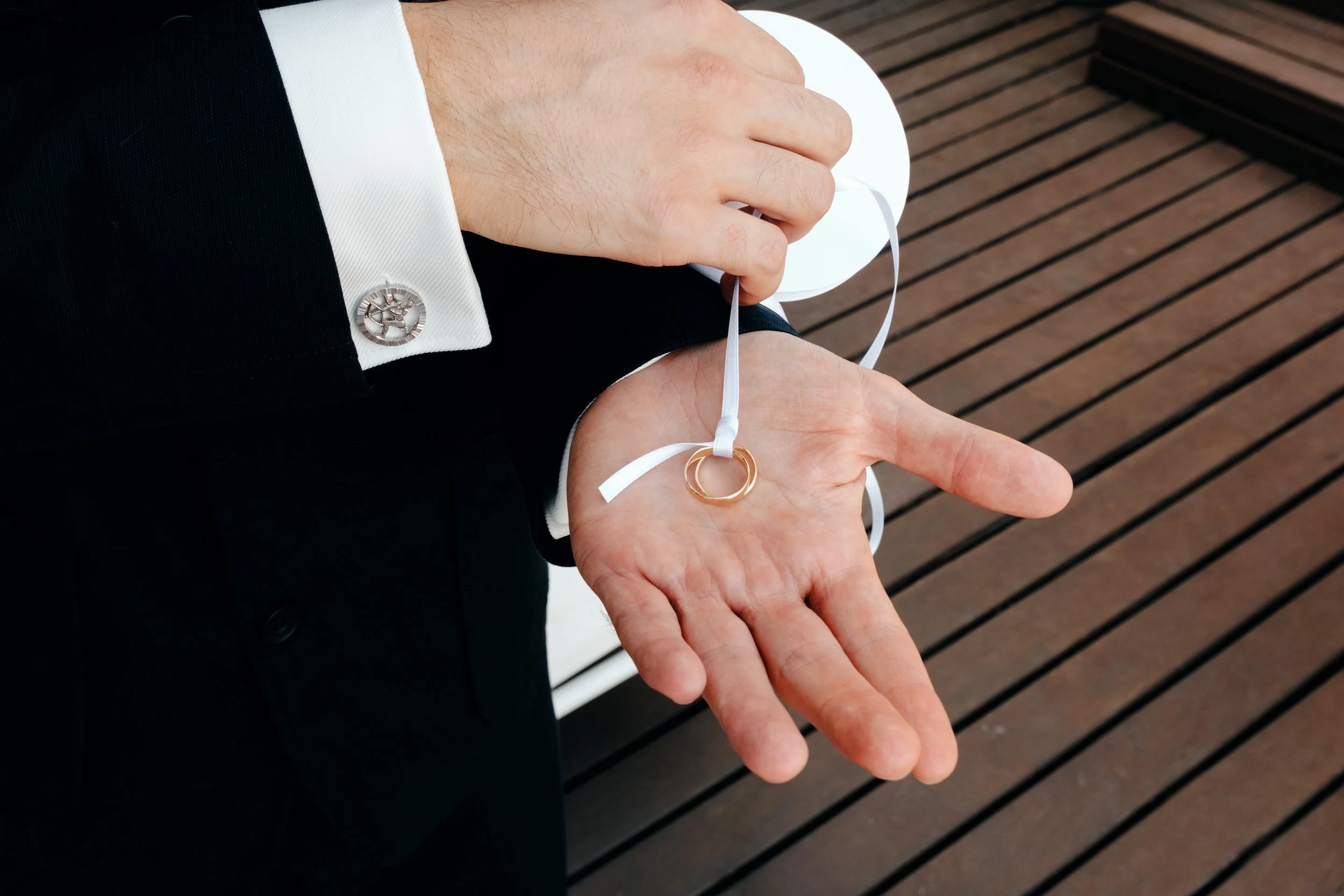 Ein Mann in formeller Kleidung hält Eheringe an einer weißen Scherenspitze.
