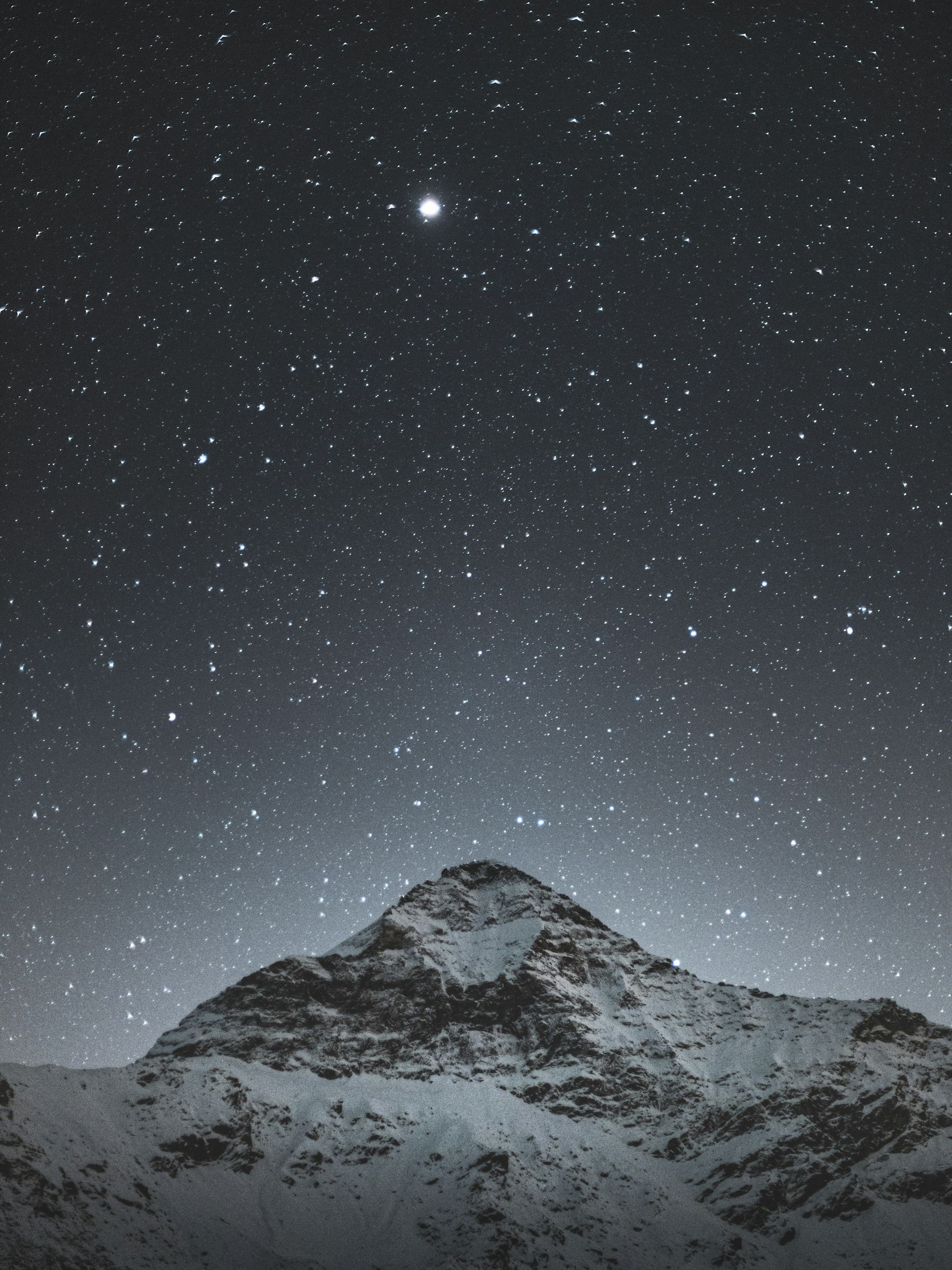 Snow-covered mountain under a starry night sky with a bright planet or star visible.